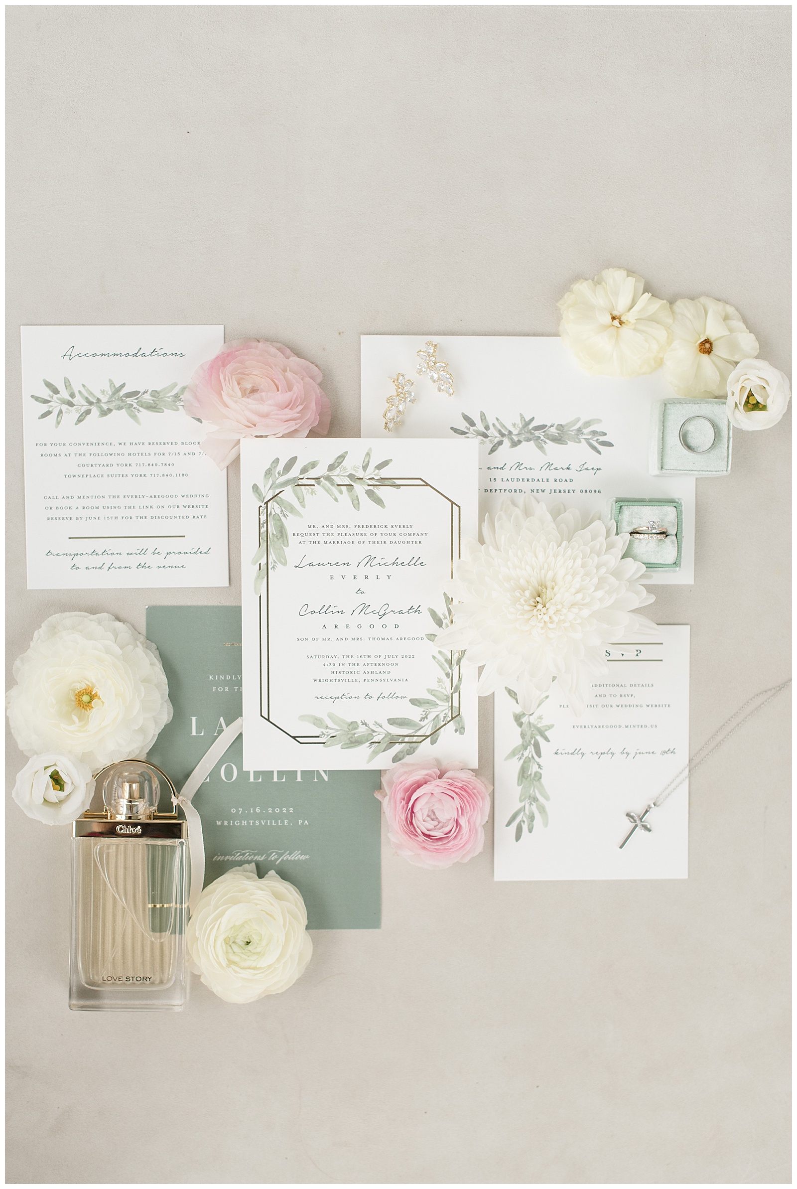 close up photo of wedding invitation surrounded by white flowers and pink roses and rings and perfume bottle in lancaster county