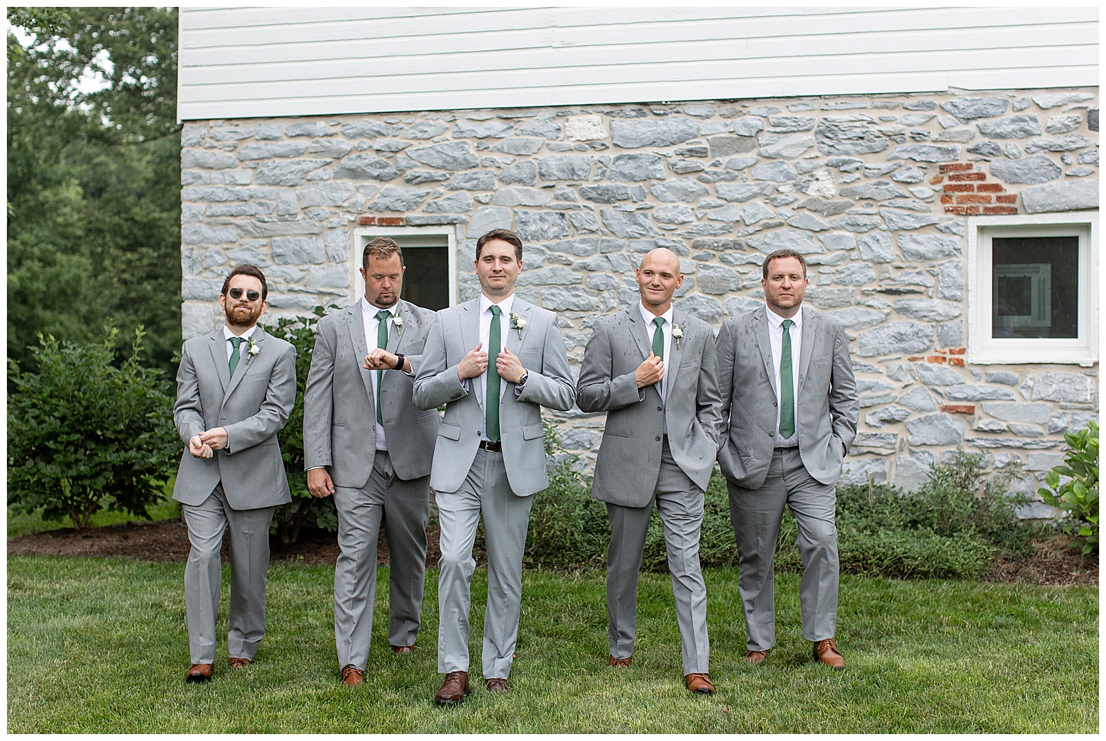 groom with his four groomsmen all in light gray suits walking towards camera by stone building at historic ashland