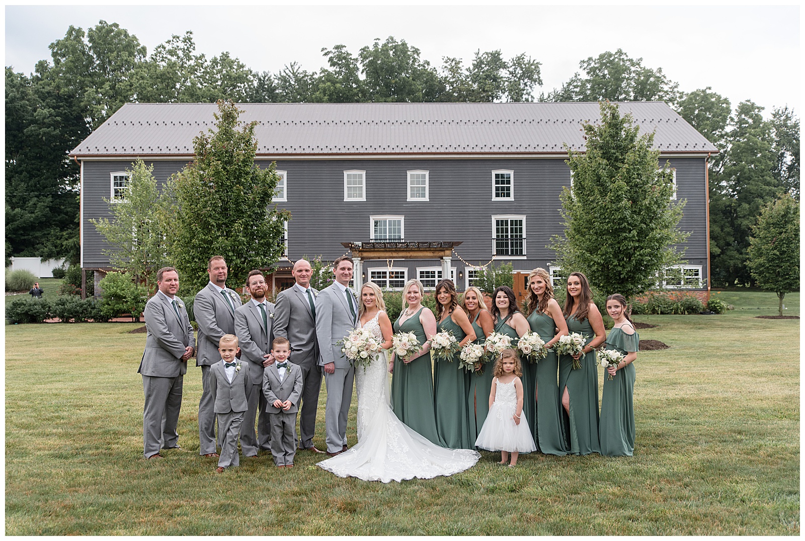 couple surrounded by their wedding party on lawn by gray barn at historic ashland