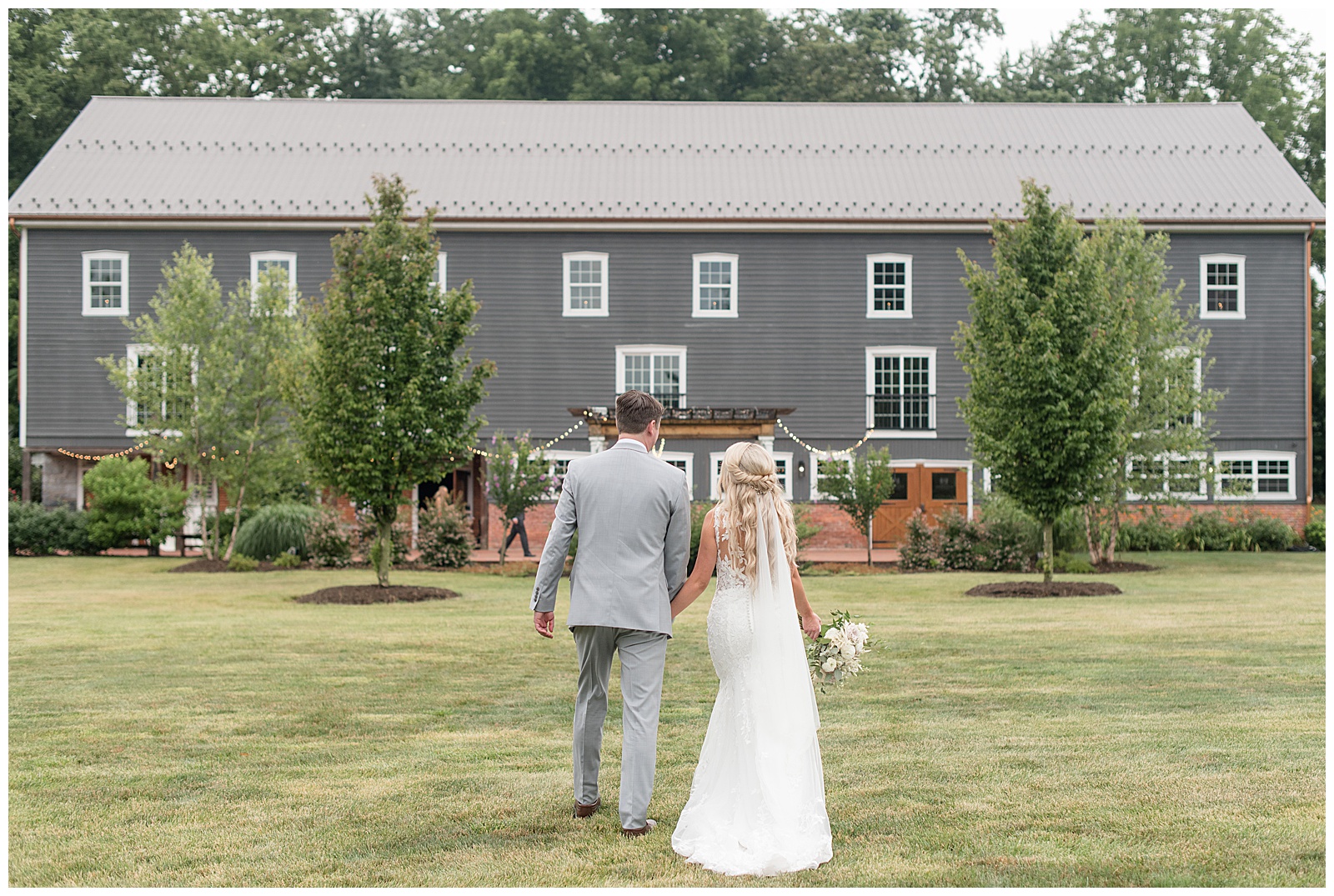bride and groom walking away from camera towards gray barn on sunny summer day in york pennsylvania