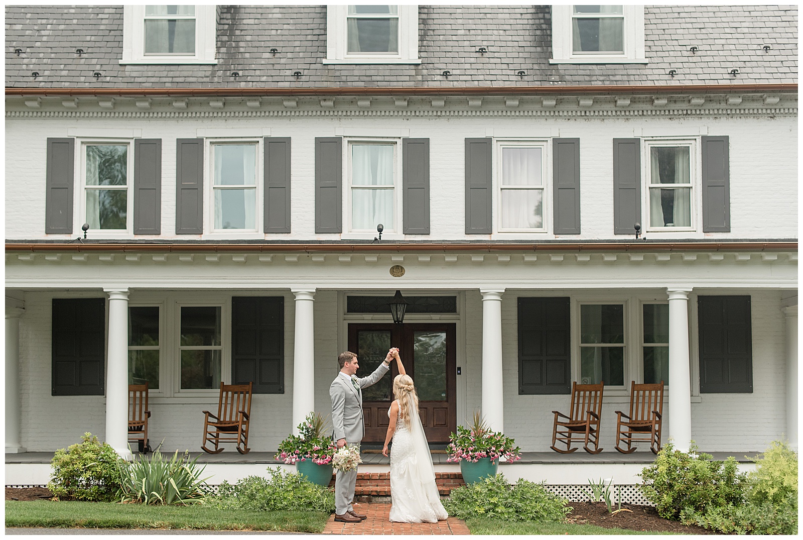 groom twirling his bride under his left hand in front of farmhouse at historic ashland