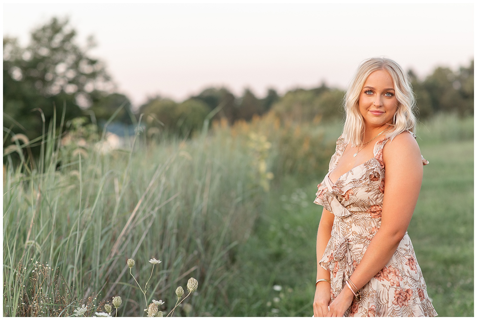 senior girl wearing cute floral dress standing by tall wildflowers at sunset at overlook park in lancaster pennsylvania