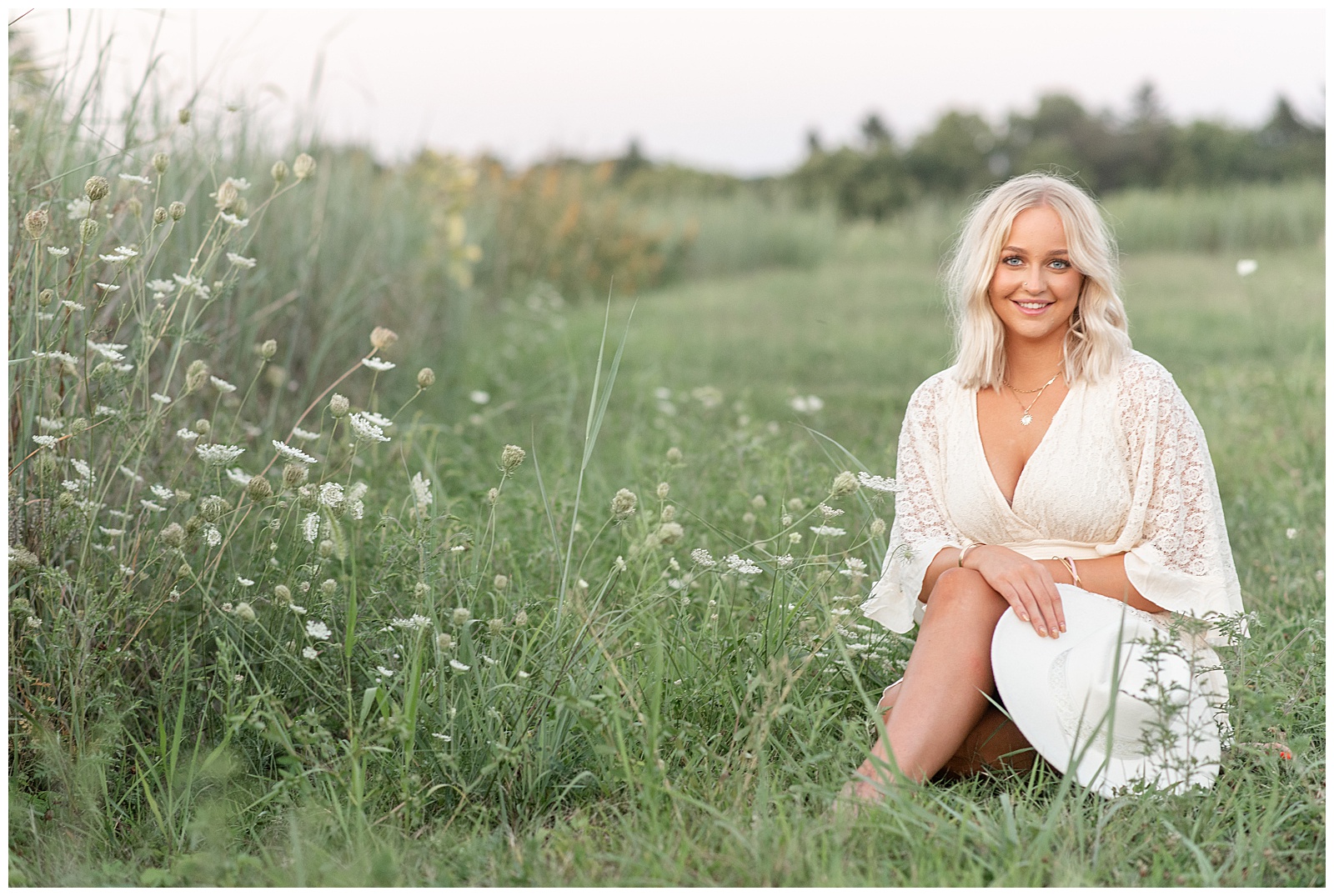 senior girl sitting in field of beautiful white wildflowers at sunset at overlook park with her legs and hands folded
