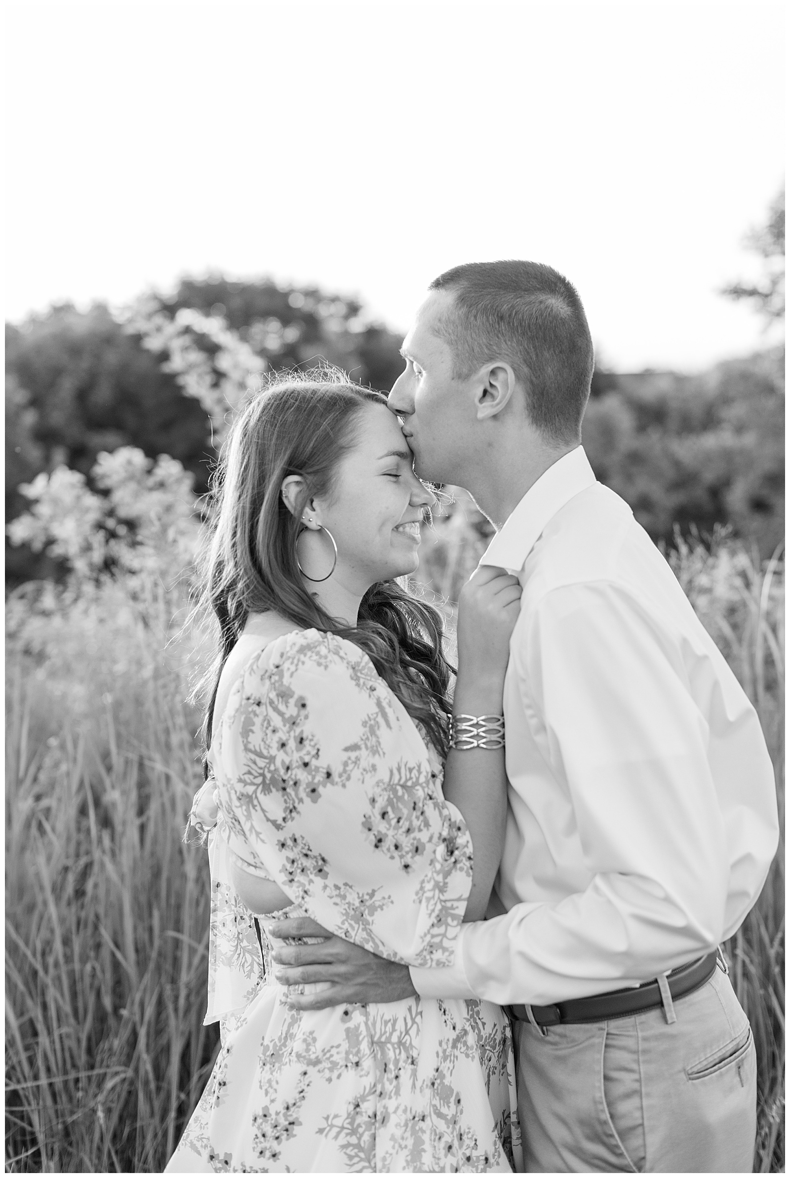 black and white photo of guy kissing girl on her forehead by tall wild grasses at overlook park