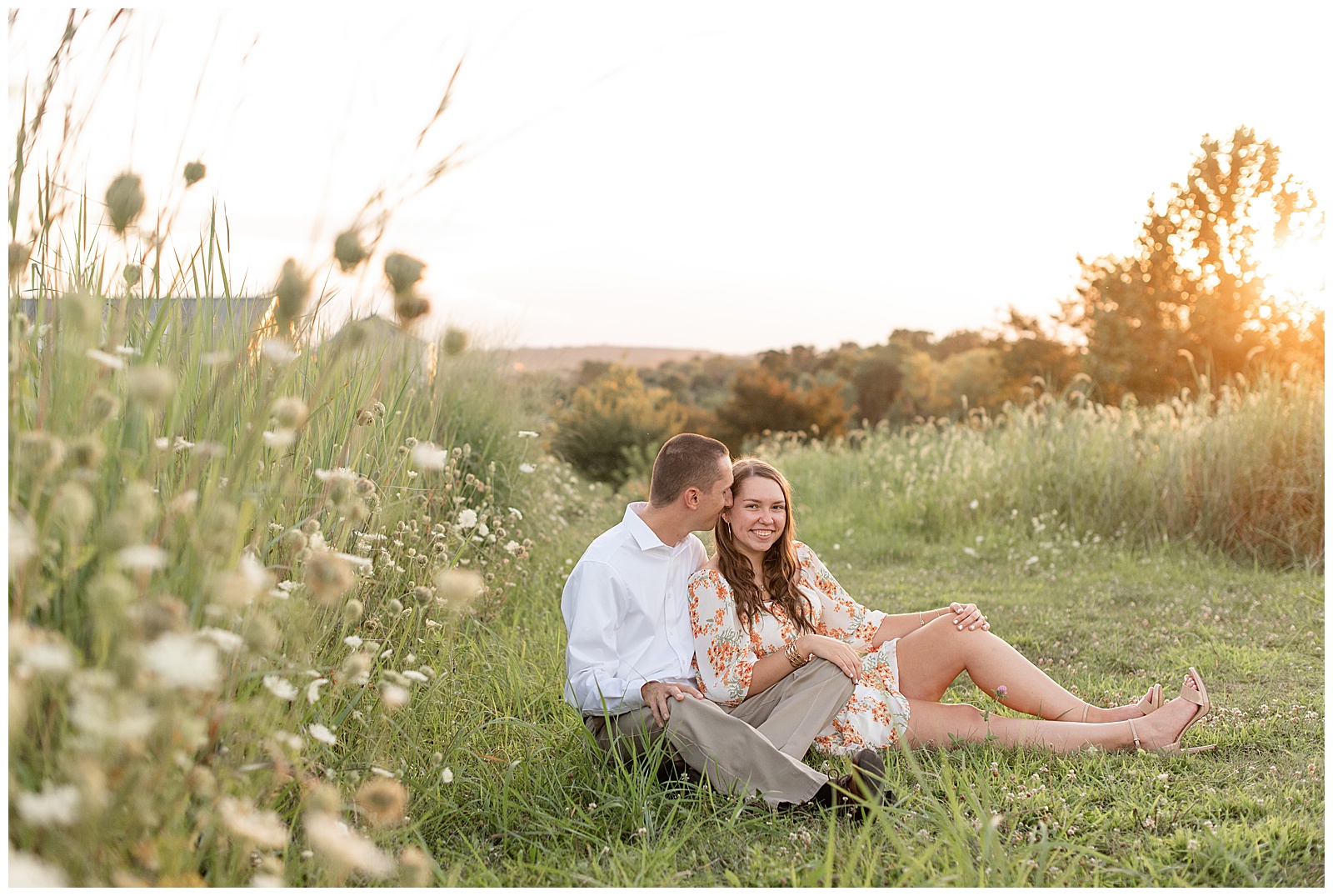 engaged couple sitting in the grass by field of wildflowers at sunset at overlook park in lancaster county