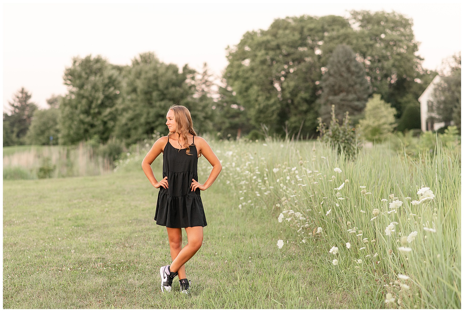 senior girl wearing little black dress with hands on hips by wildflowers at overlook park