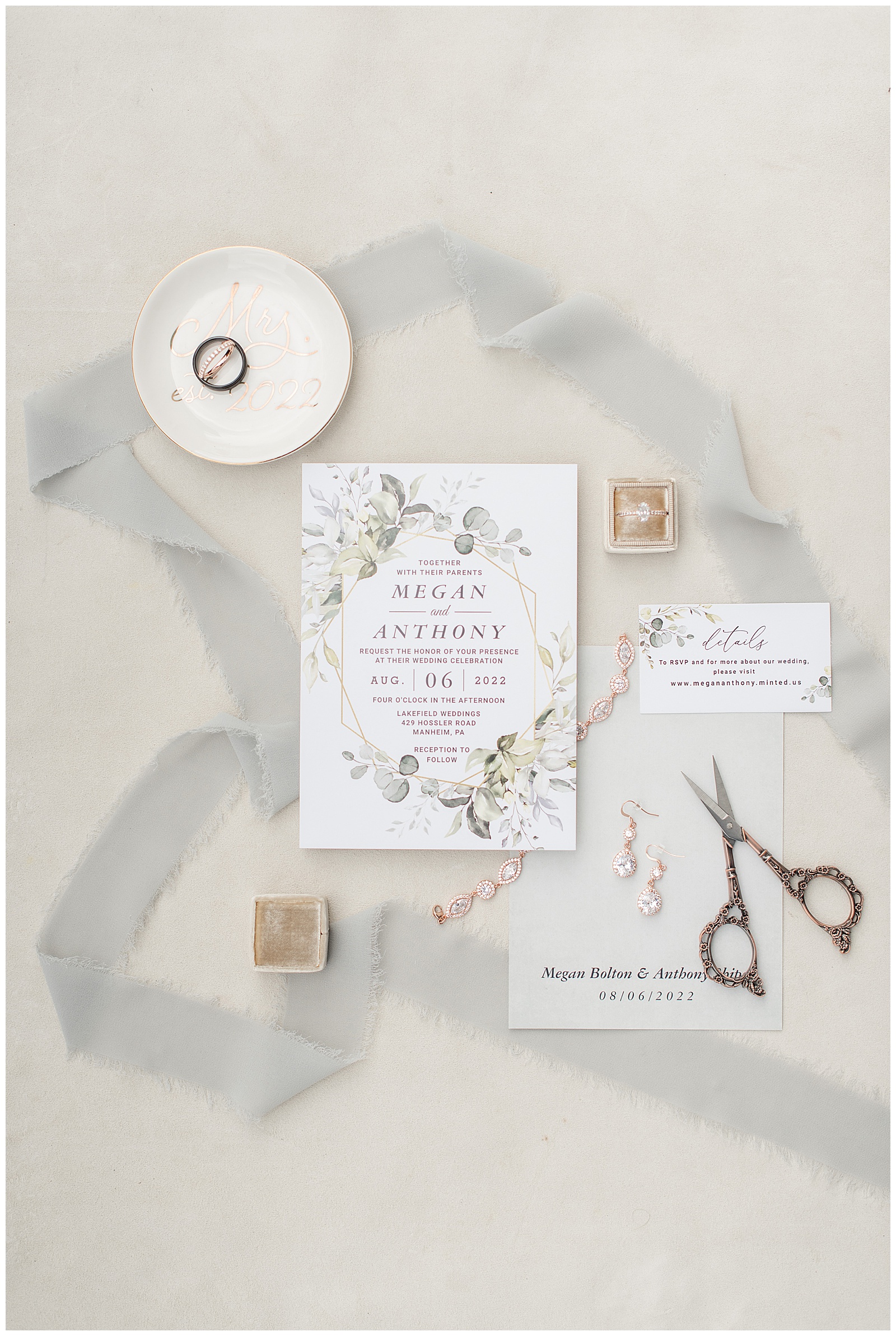 wedding invitation surrounded by gray ribbon, antique scissors, wedding rings and jewelry at lakefield weddings