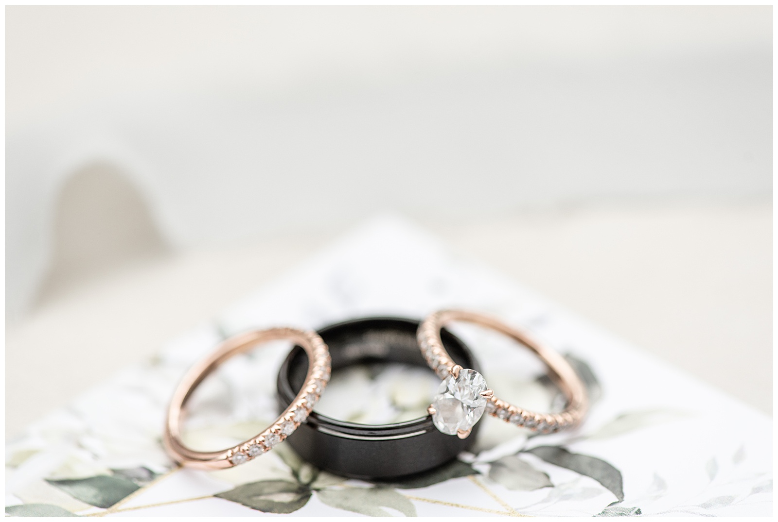 gold diamond engagement ring and diamond wedding band resting on groom's black wedding ring at lakefield weddings