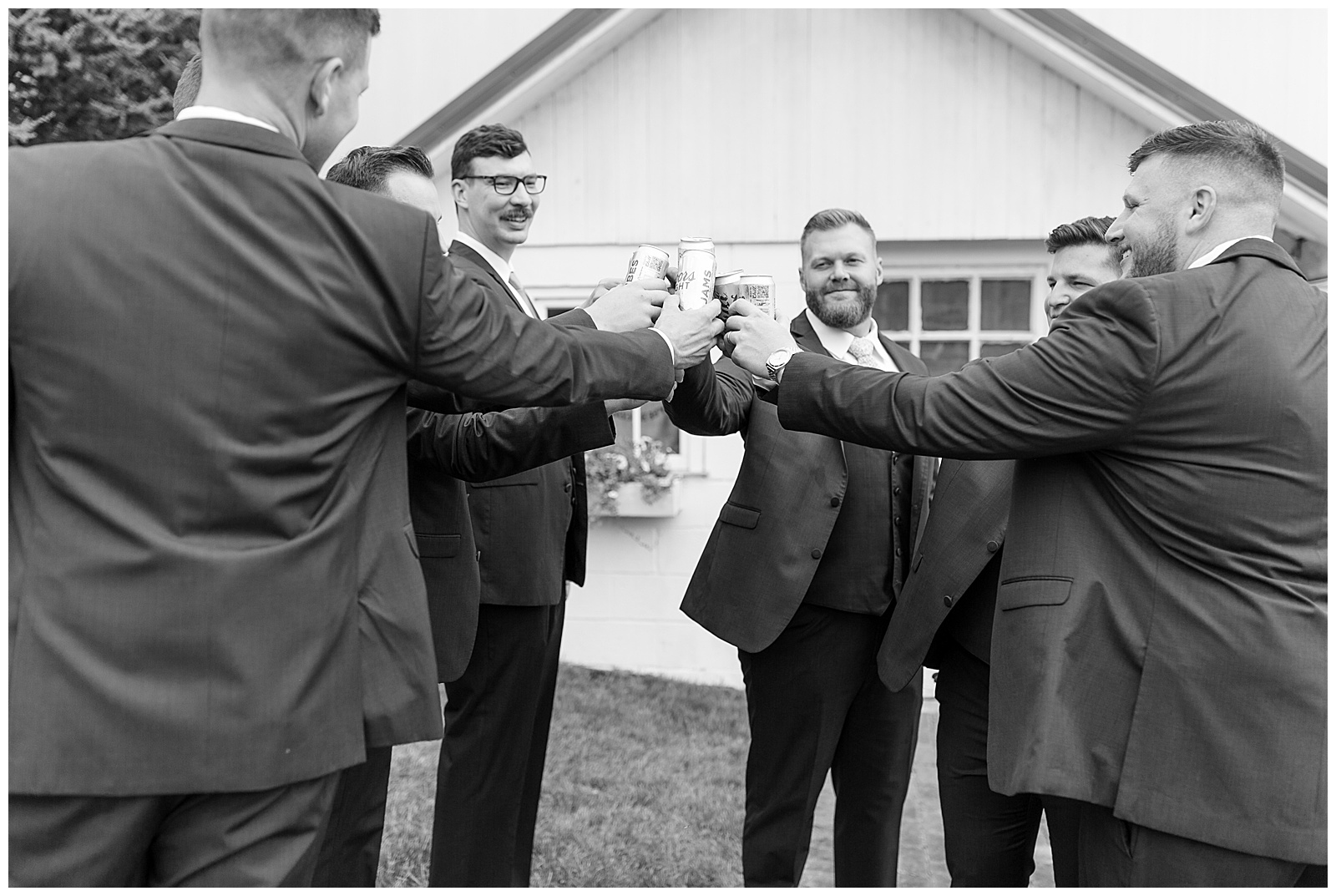 black and white photo of groom and groomsmen all toasting cans of beer at lakefield weddings