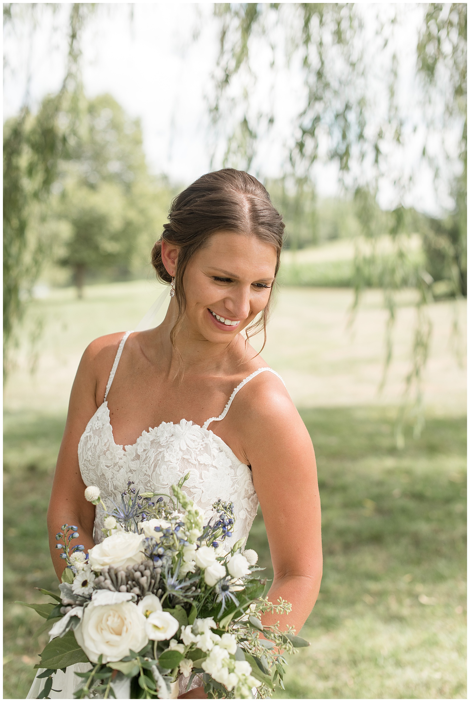 bride smiling as she looks down holding her white bouquet of flowers at lakefield weddings