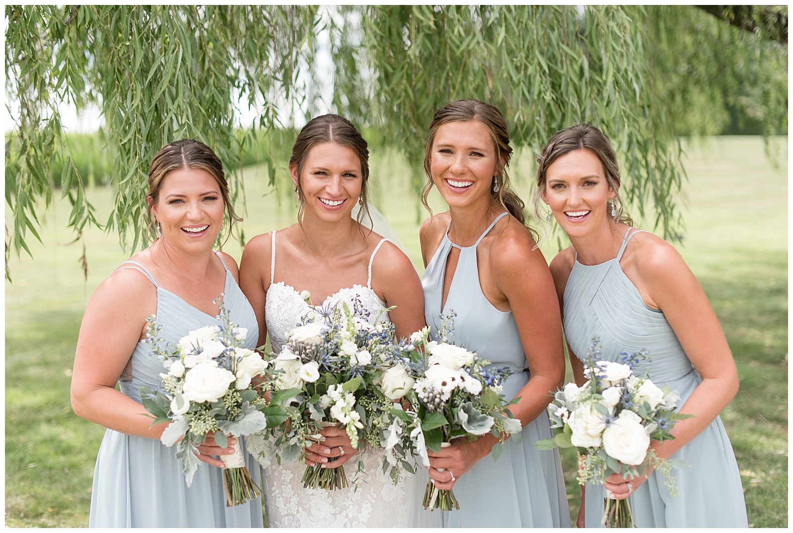 bride in white spaghetti strap gown standing with three bridesmaids in pale blue gowns at lakefield weddings