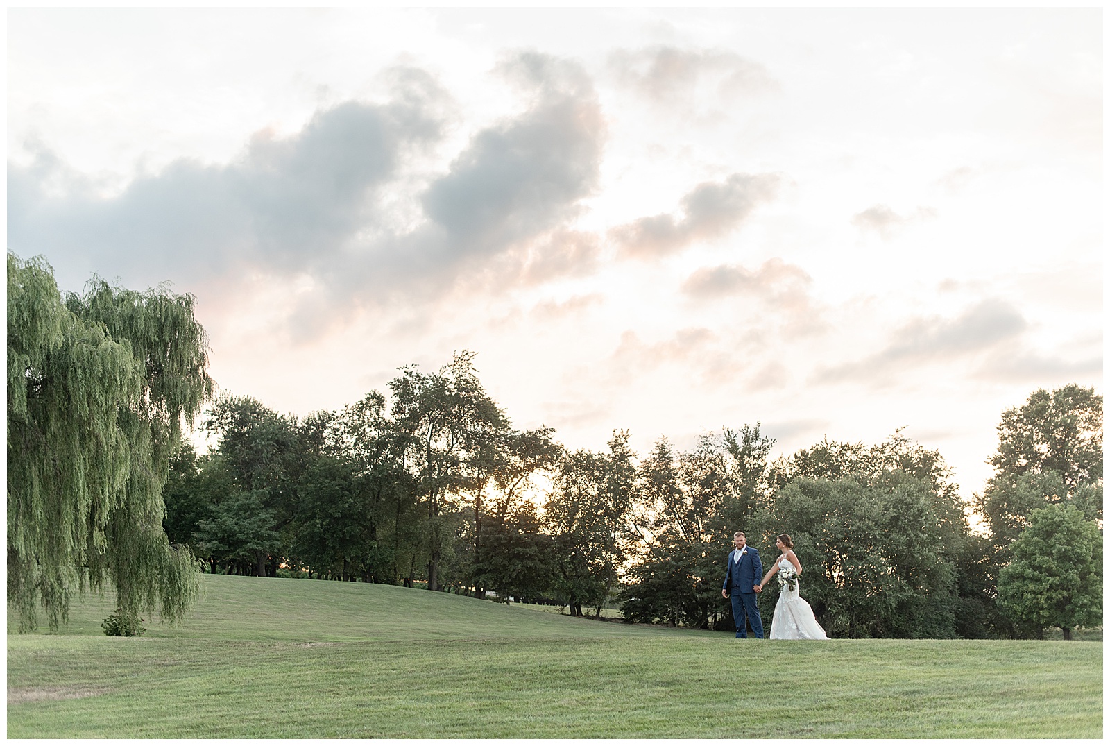 bride and groom walking up tall hill with trees and sunset behind them at lakefield weddings in manheim pennsylvania