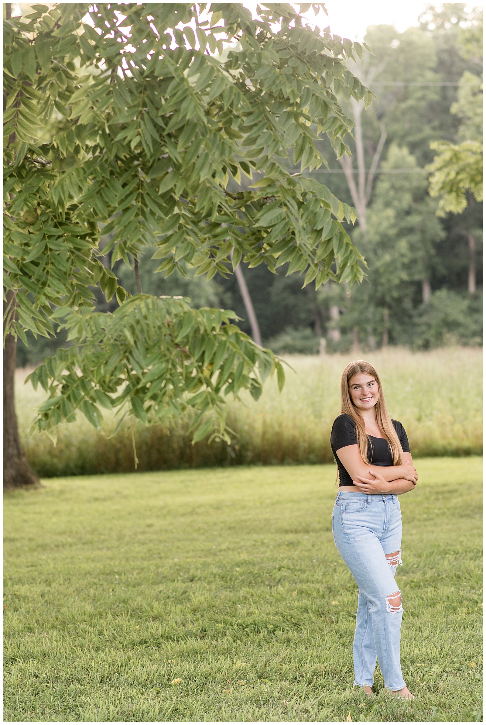 senior girl with arms folded and legs crossed by tree at hibernia park in coatesville pennsylvania