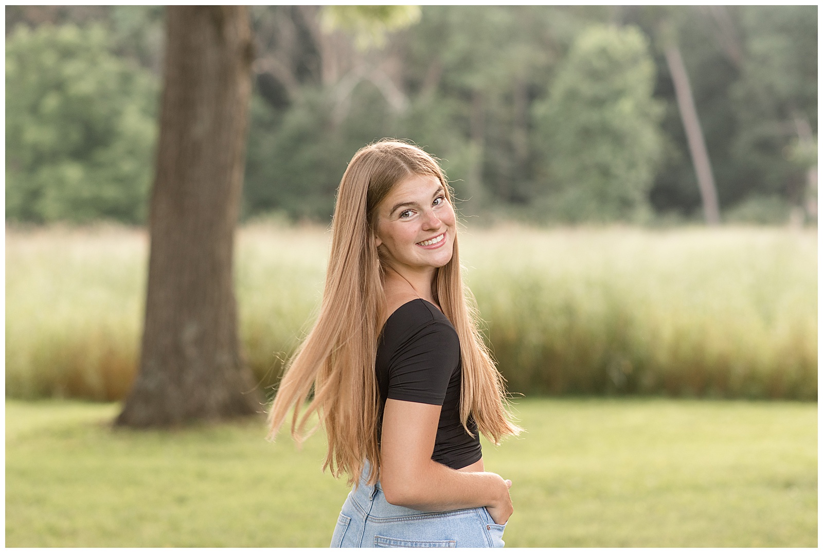 senior girl turning back and looking over right shoulder as she smiles at park in chester county pennsylvania