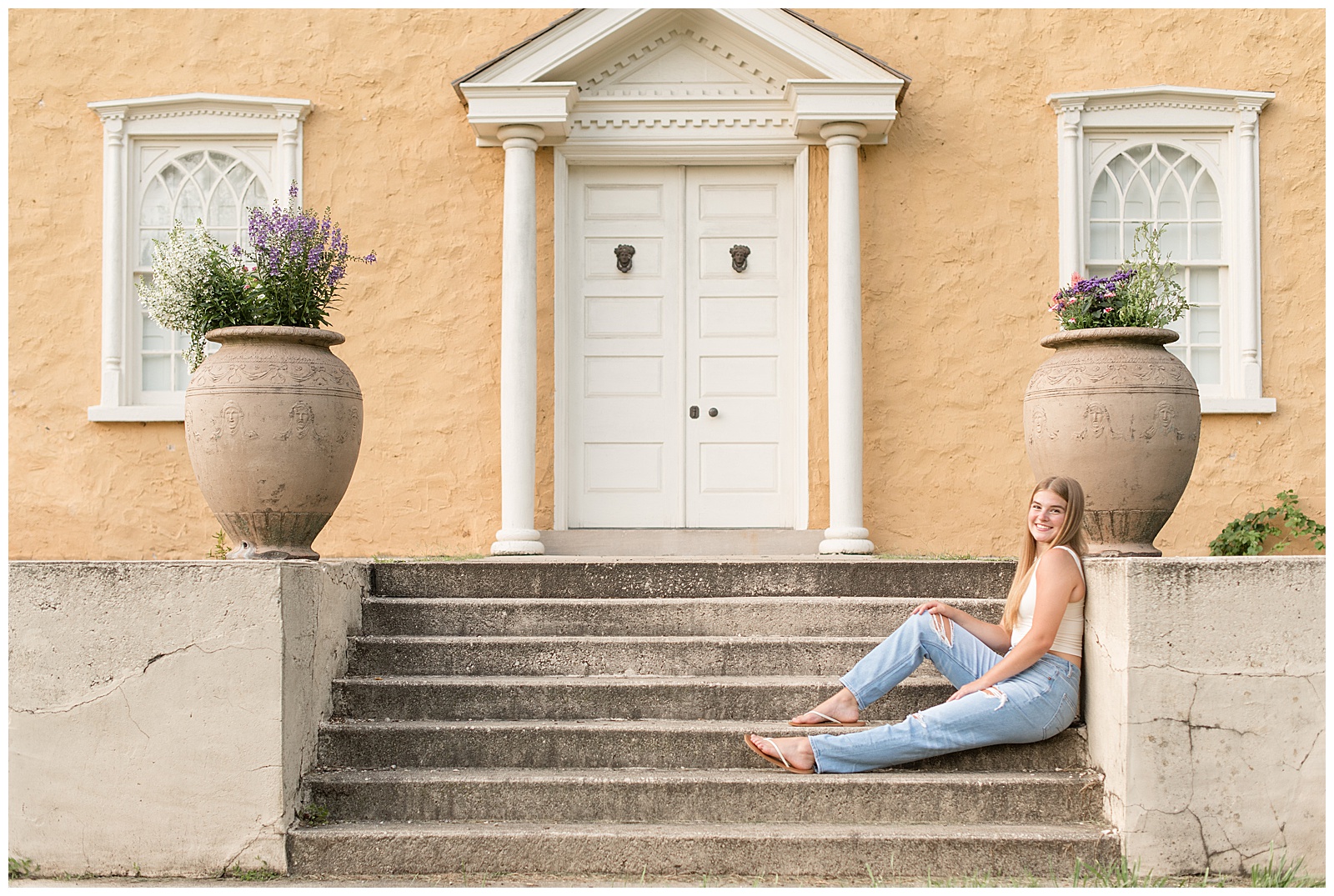 senior girl sitting on concrete steps of historic peach colored building at hibernia park in pennsylvania