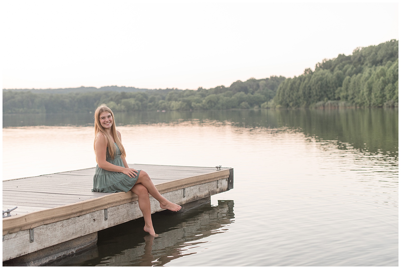 senior girl in cute green summer dress sitting on dock with legs crossed by lake at hibernia park
