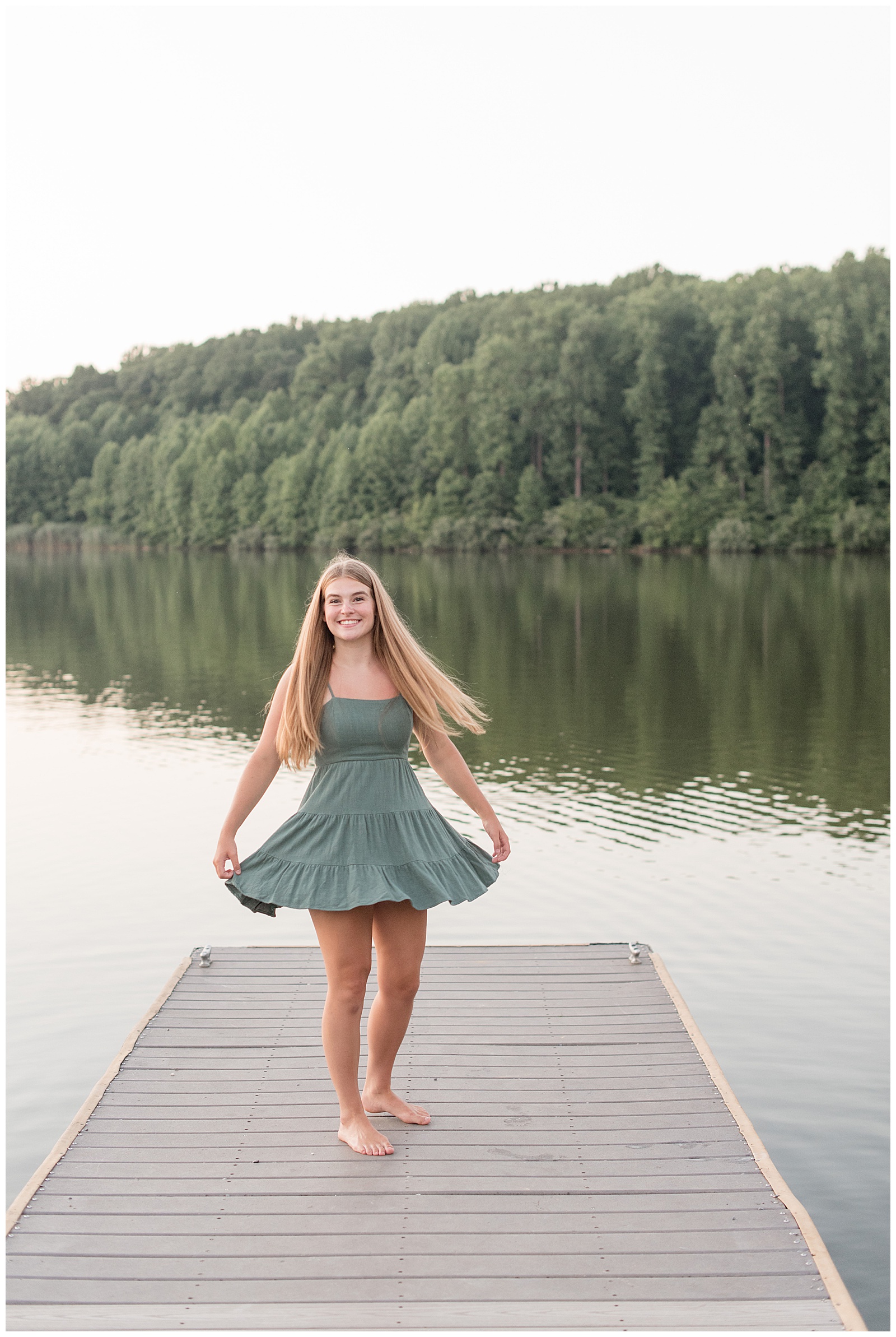 senior girl holding edges of green dress and flaring it out on dock by lake at hibernia park