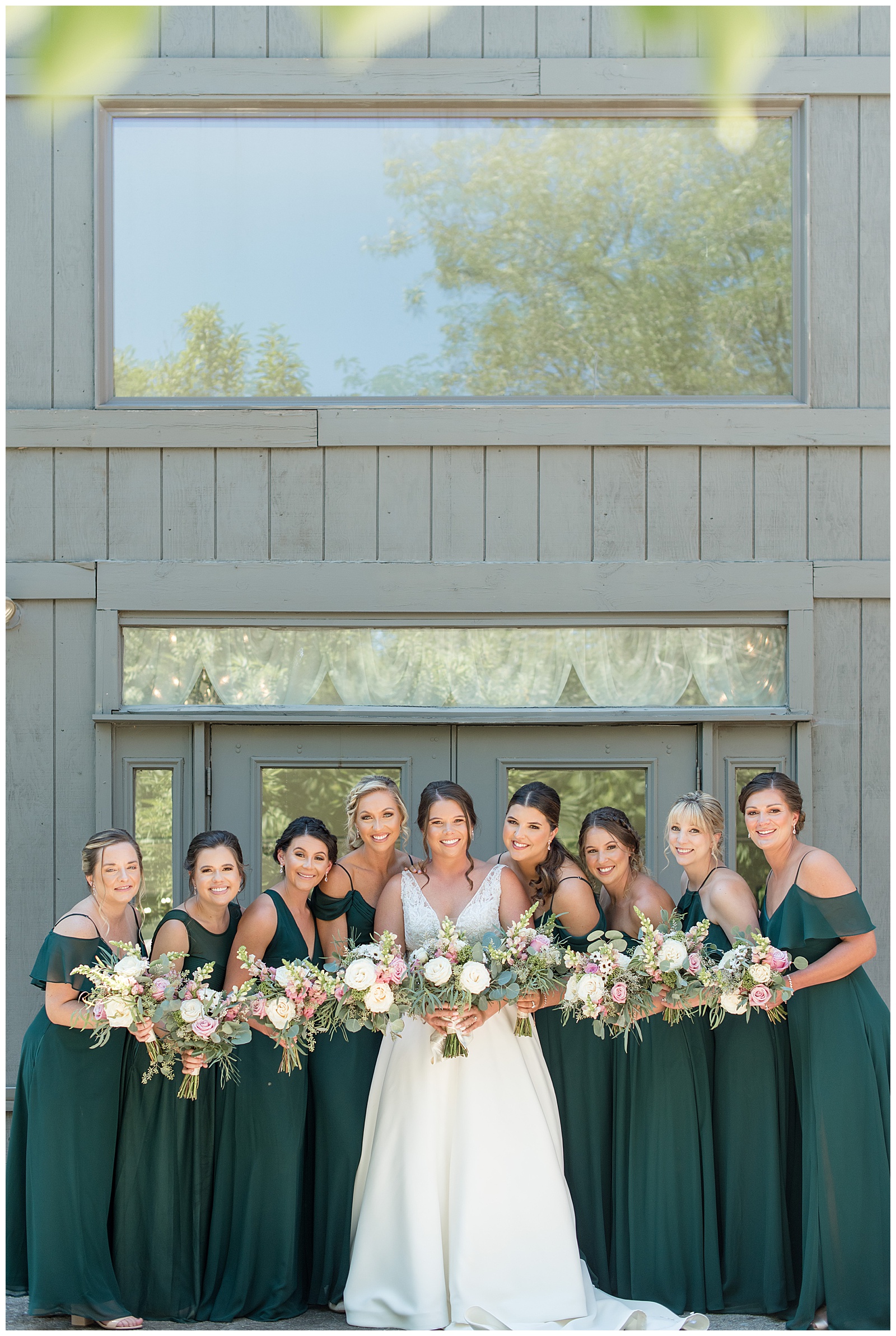bride with her eight bridesmaids all leaning in with their bouquets at the manor at mountain view