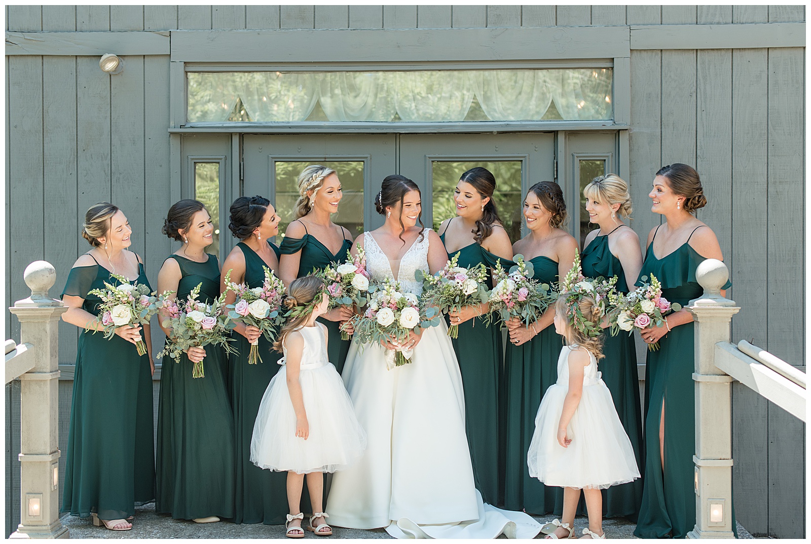 bride with her flower girls and bridesmaids all looking at each other and smiling at the manor at mountain view