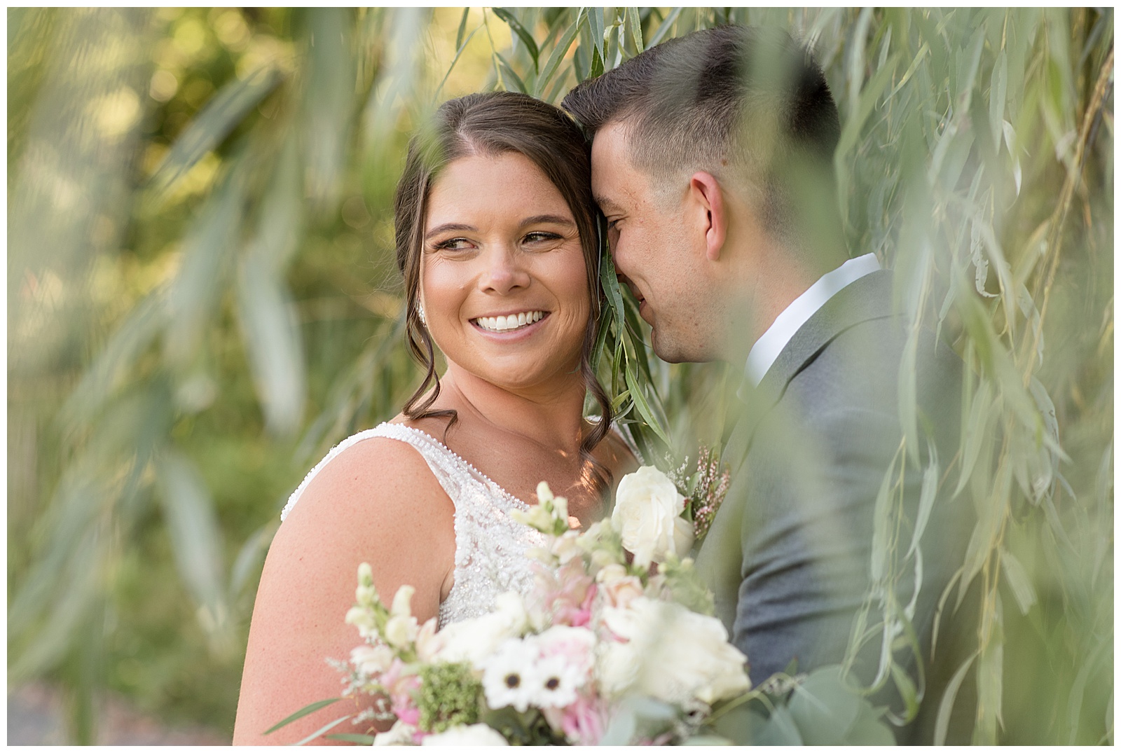 close up photo of bride smiling and looking right as her groom nuzzles into her left cheek under willow tree in harrisburg pennsylvania