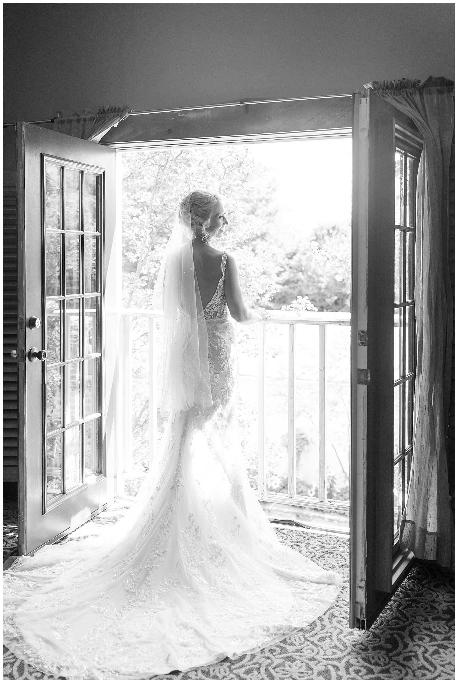 black of white photo of back of bride in gown with long train as she looks out over balcony at the inn at leola village