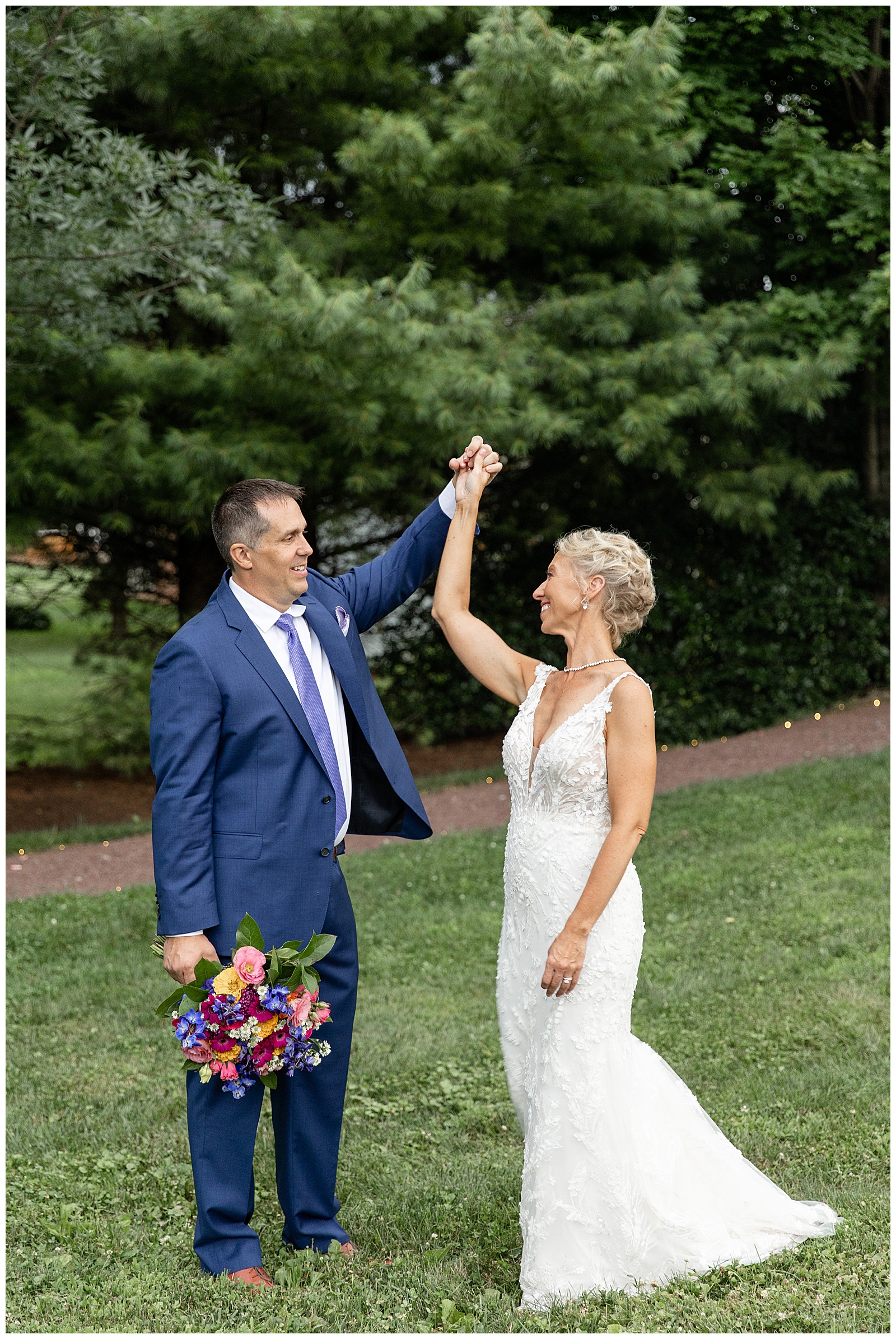 groom twirling his bride under his left hand as he holds her bouquet in his right hand at the inn at leola village