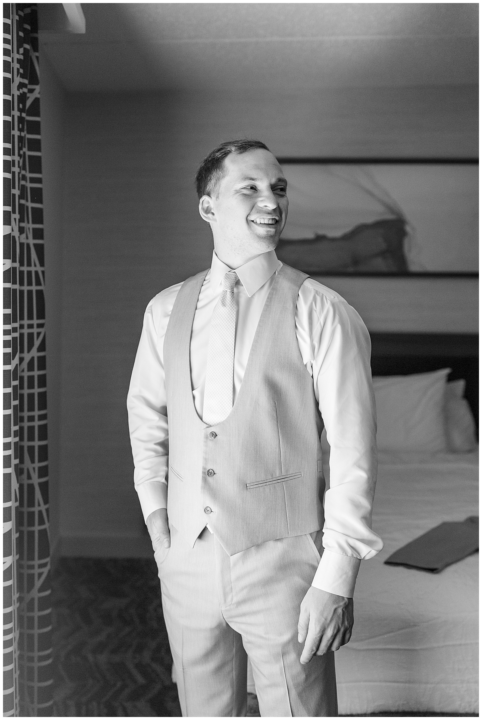 black and white photo of groom getting read and looking over his left shoulder in hotel room in long island new york