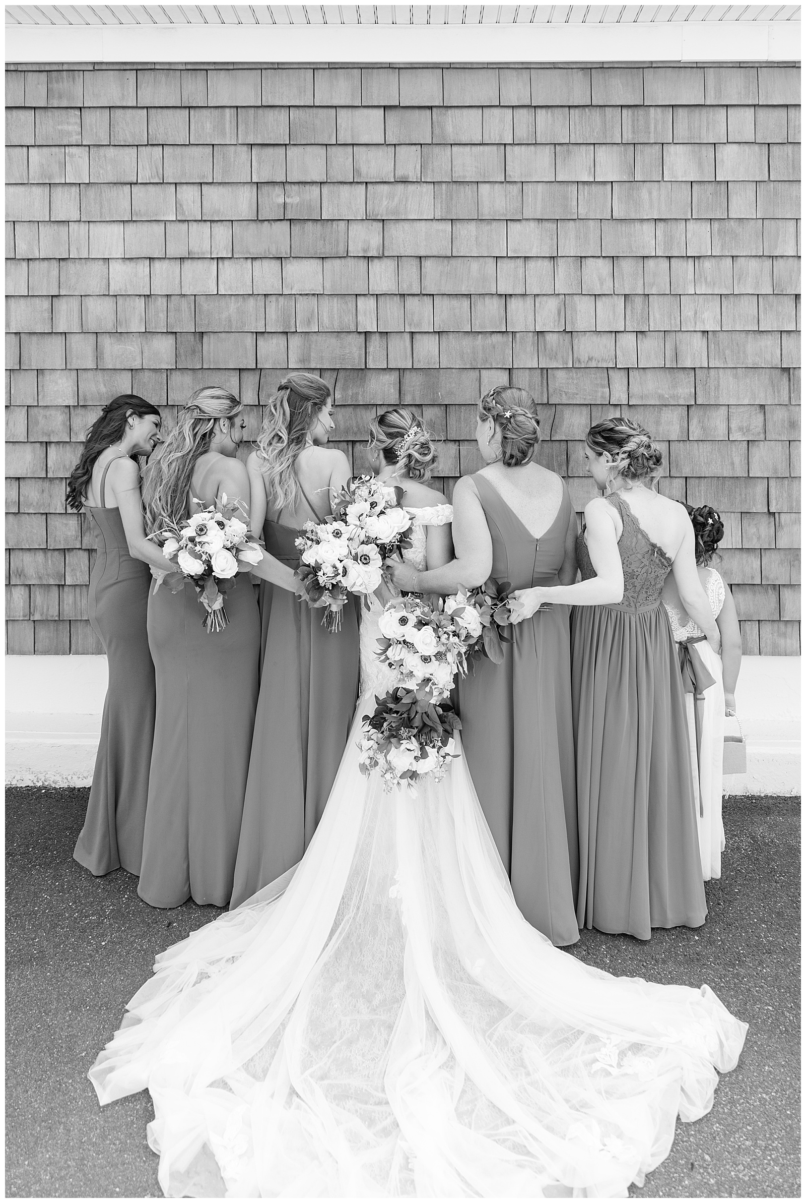 black and white photo of bride and bridesmaids with their backs toward camera and arms around each other at captain bill's in new york
