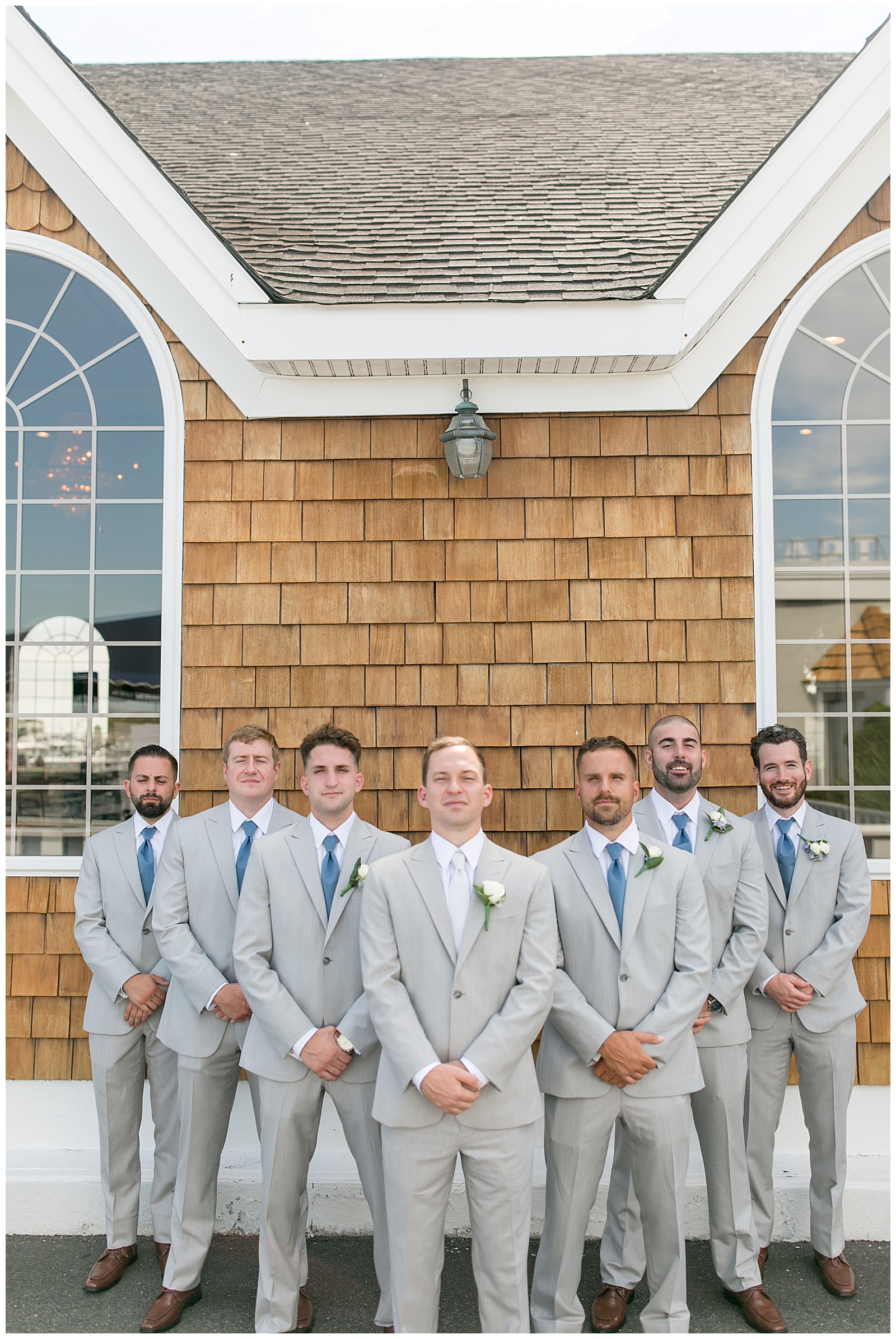 groom with his six groomsmen all in light gray suits with blue ties standing outside tan building at captain bill's in bay shore, new york