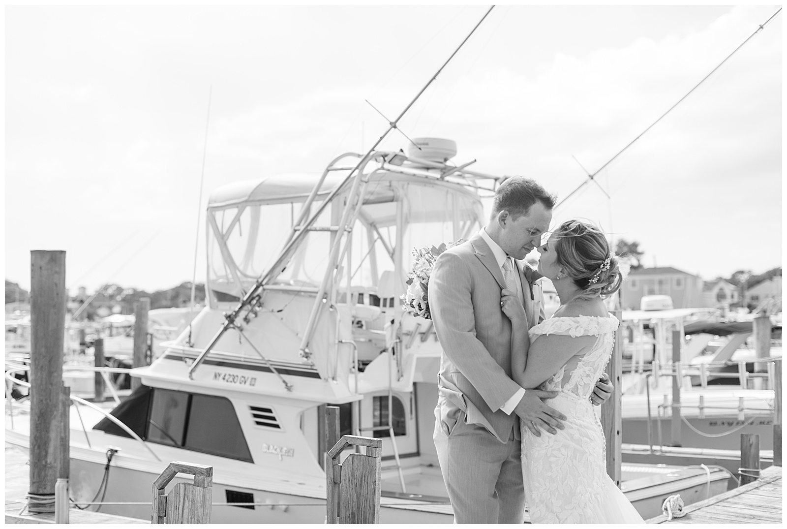 black and white photo of couple almost kissing with large yacht behind them on summer day in bay shore new york