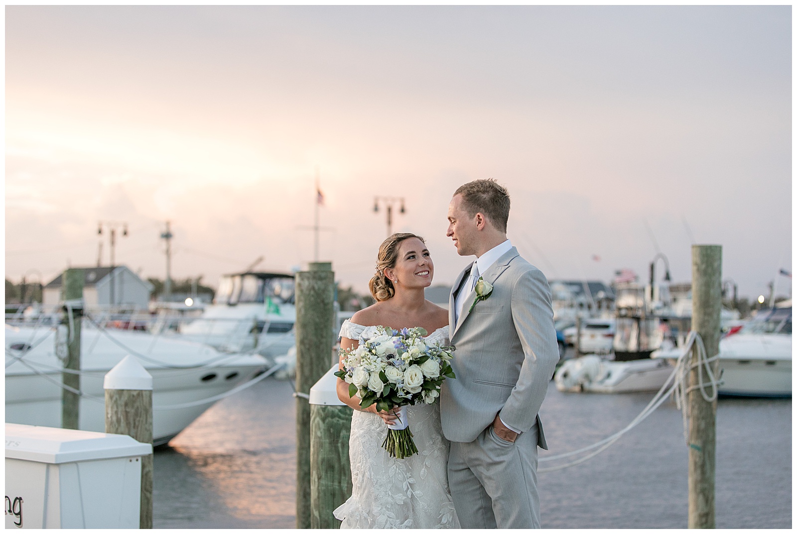 bride and groom looking at one another smiling with harbor of boats behind them at sunset in new york