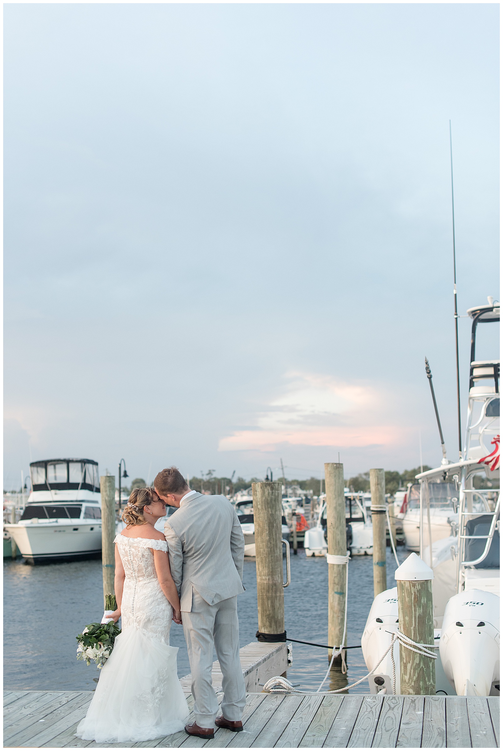 couple kissing with their backs toward the camera on dock with boats around them in bay shore new york
