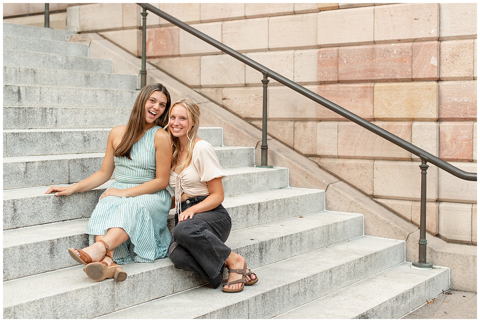 two senior girls sitting on concrete steps of the lancaster county courthouse on sunny summer evening in lancaster pennsylvania