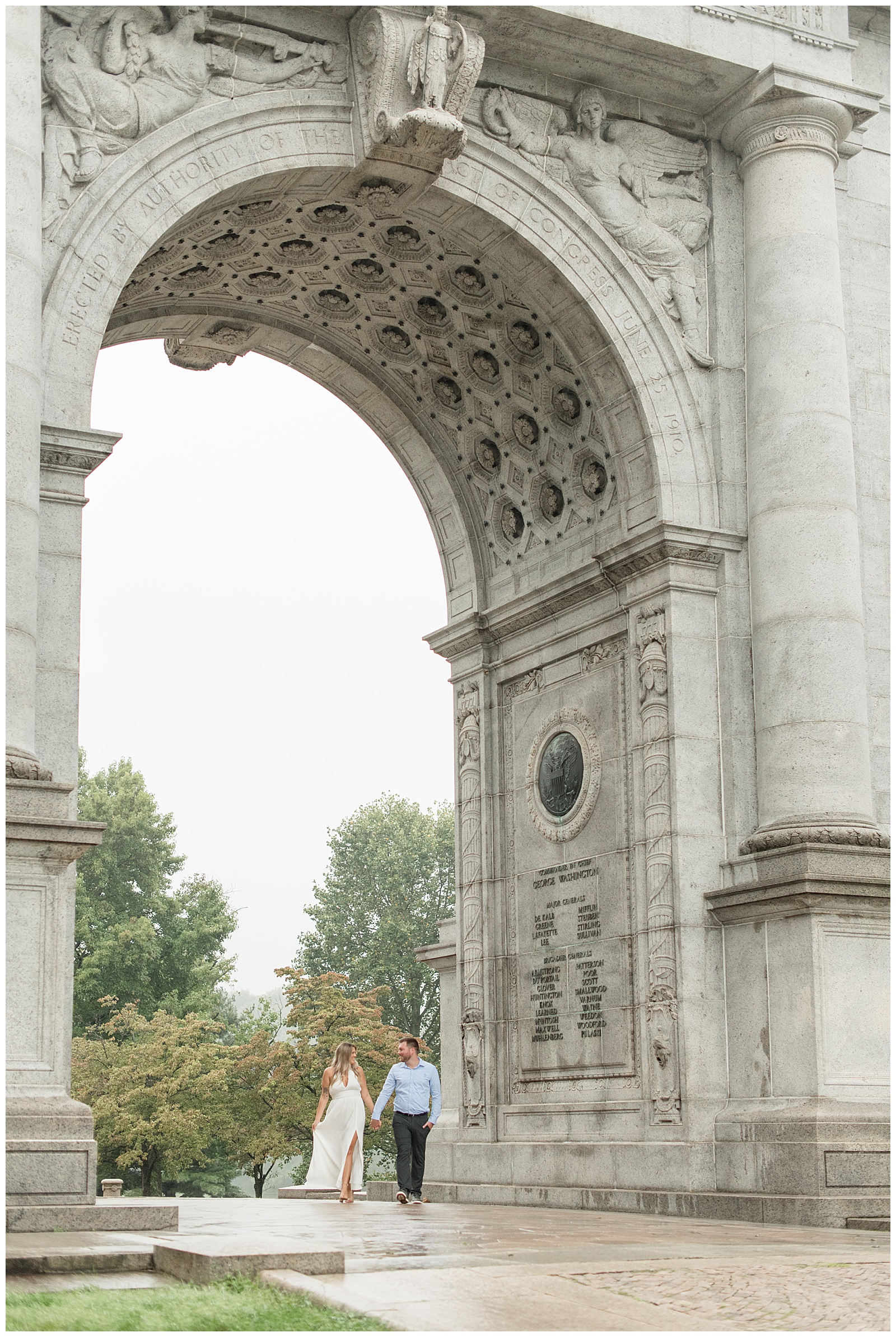 engaged couple holding hands and smiling at one another under detailed granite arch at national memorial arch