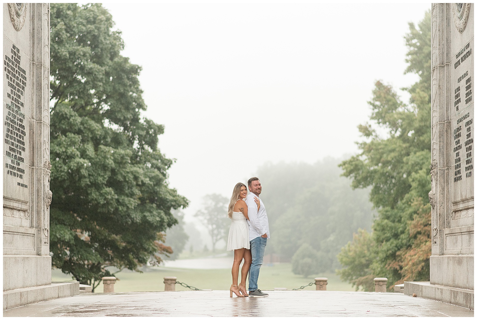 woman in short white dress hugging her guy wearing white button-up shirt and blue jeans from behind with fog behind them at valley forge