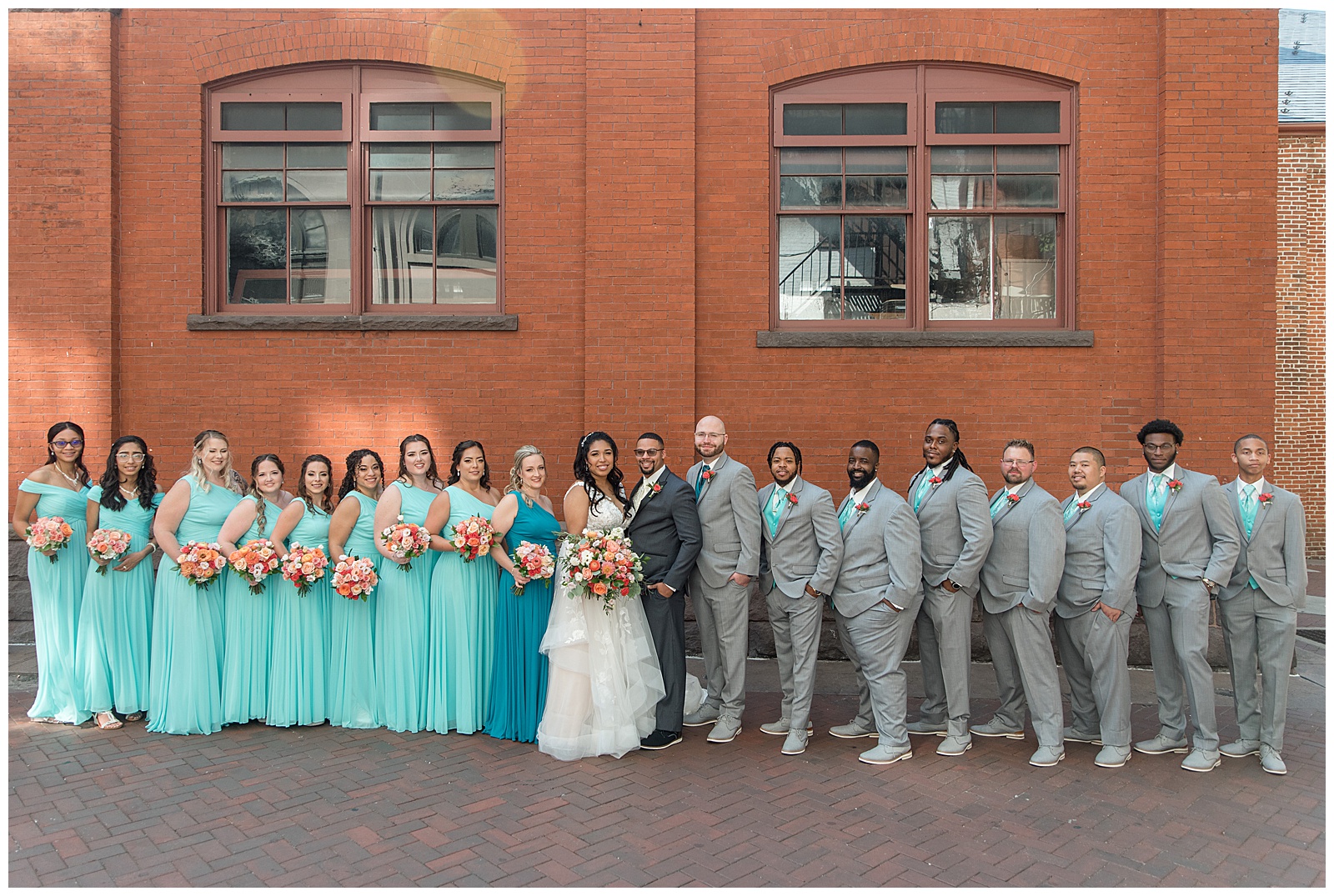 bride and groom surrounded by their bridal party all wearing light gray suits and teal gowns by lancaster's central market