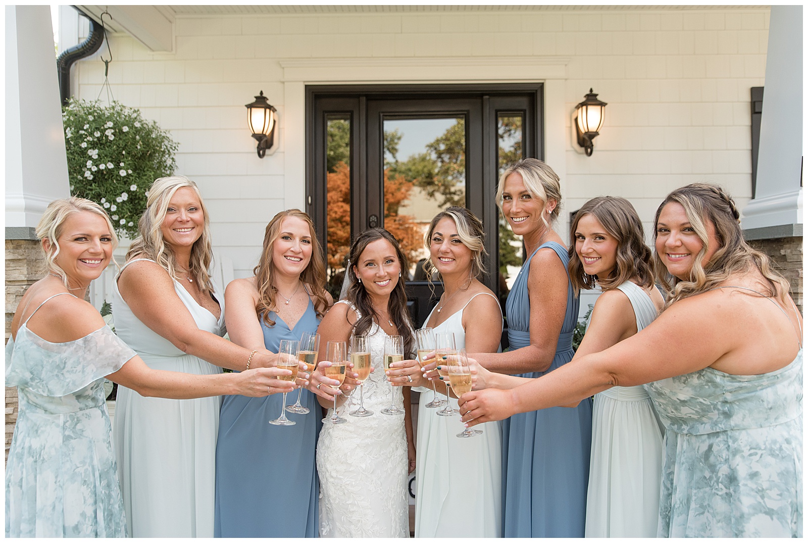 bride in white sleeveless gown surrounded by bridesmaids in different shades of blue dresses with glasses of champagne in new jersey
