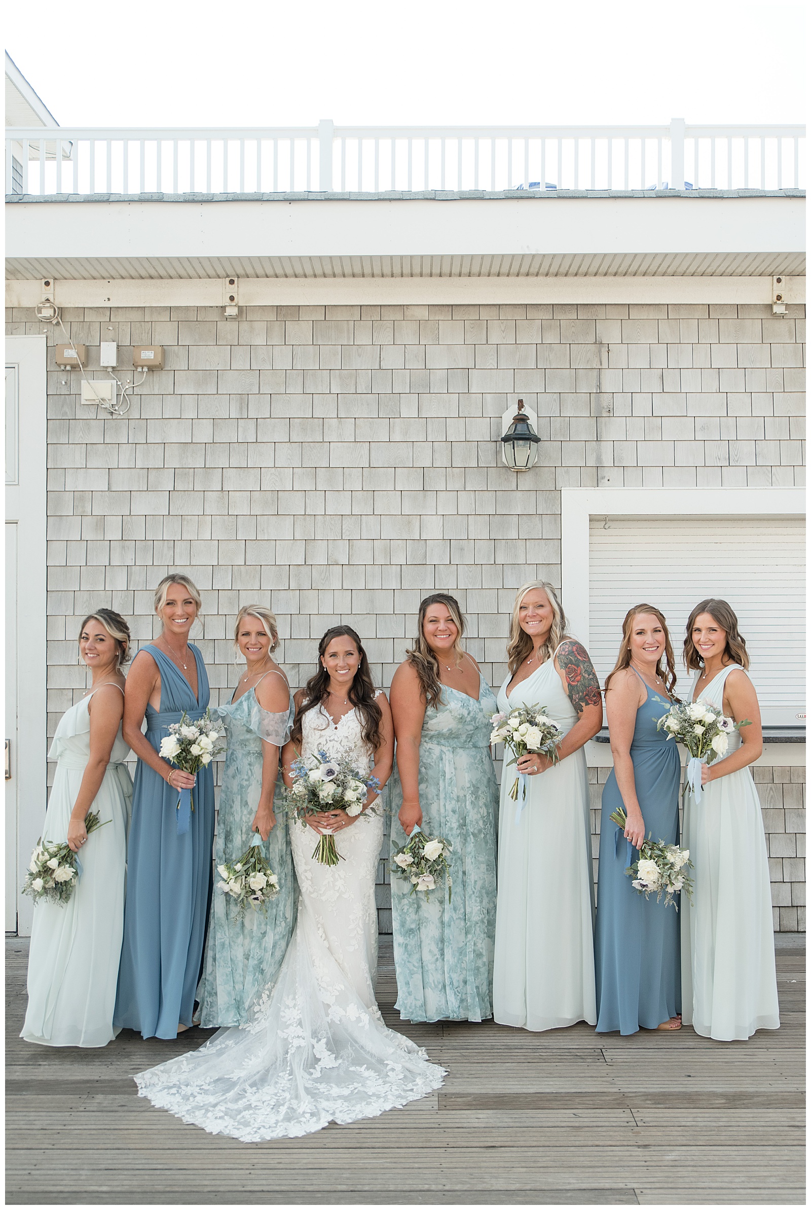 bride surrounded by her seven bridesmaids standing in various directions by gray building in new jersey