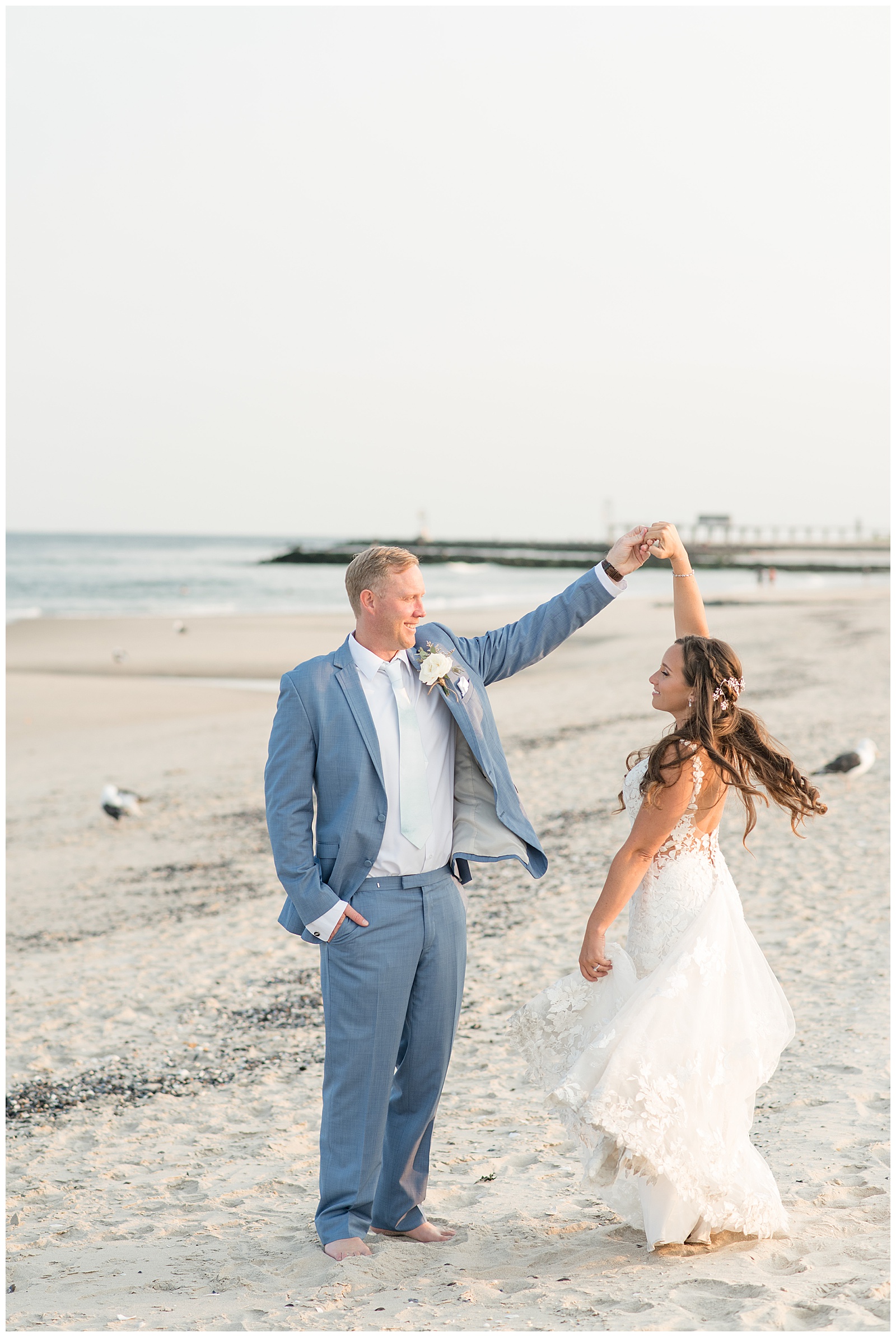 groom twirling his bride under his left hand as she flares out her dress train on the beach in new jersey
