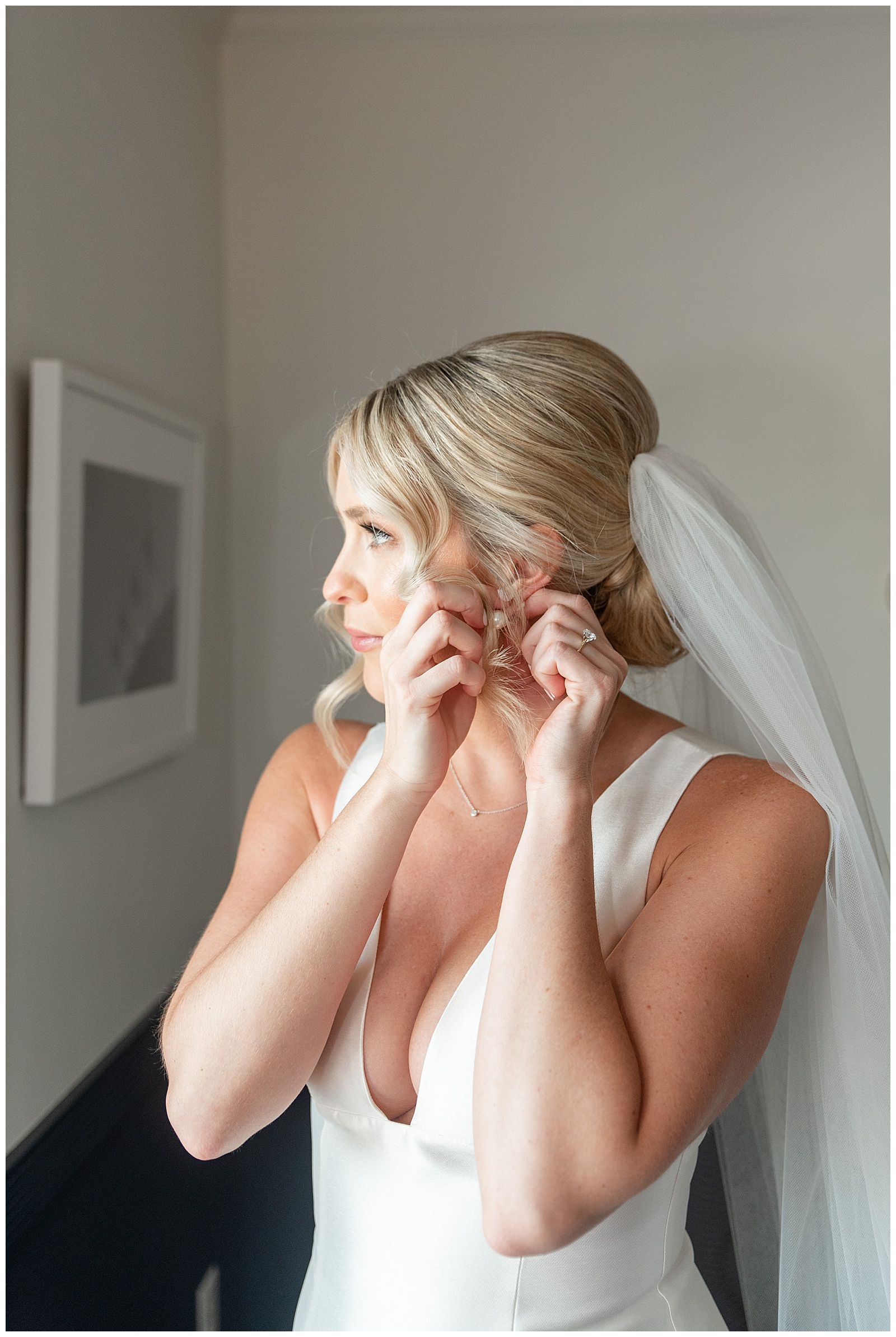 bride putting her left earring into her ear with sleeveless white wedding gown with white veil in tilghman island