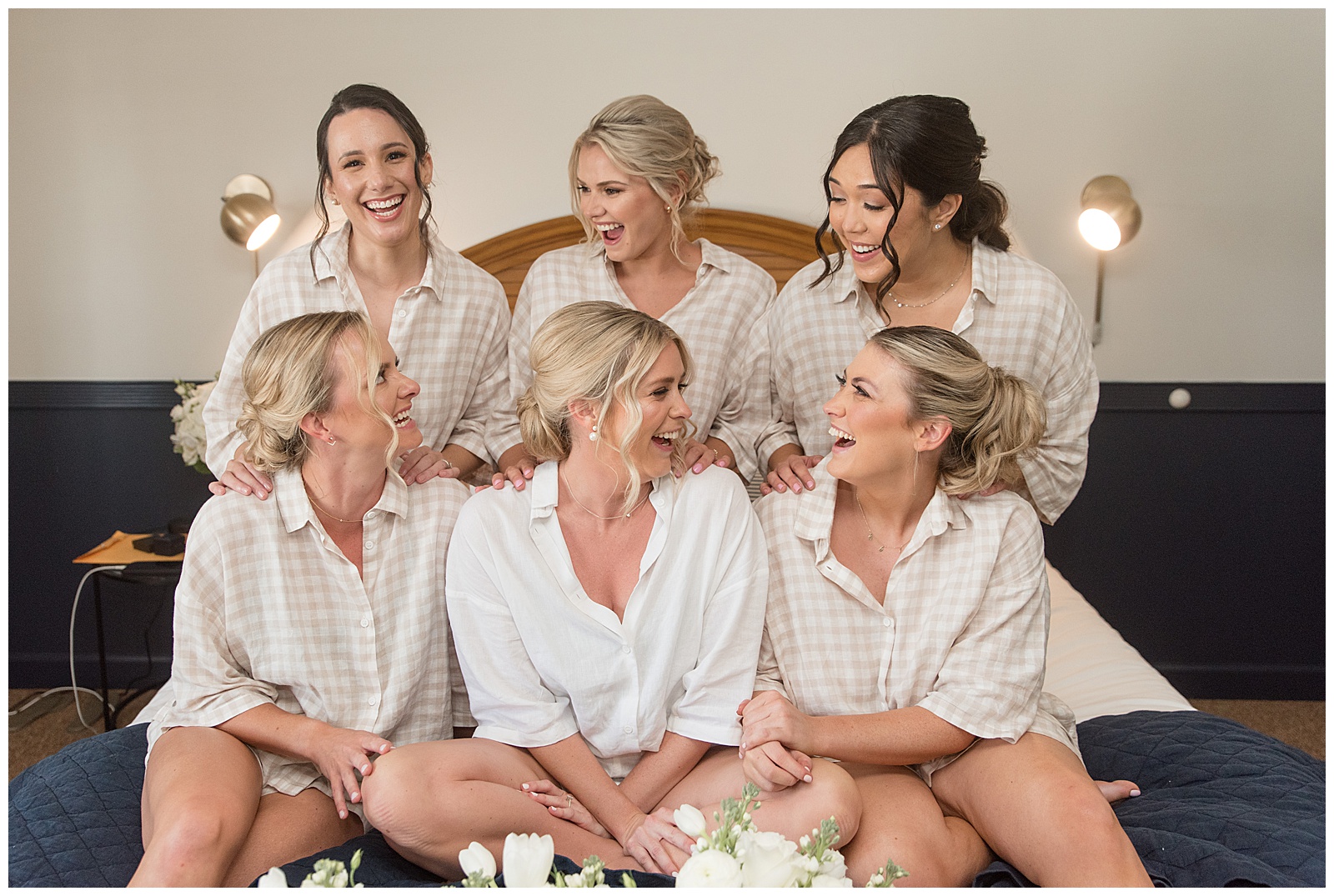 bride surrounded by her five bridesmaids all in white robes and sitting on bed at wylder hotel in tilghman island