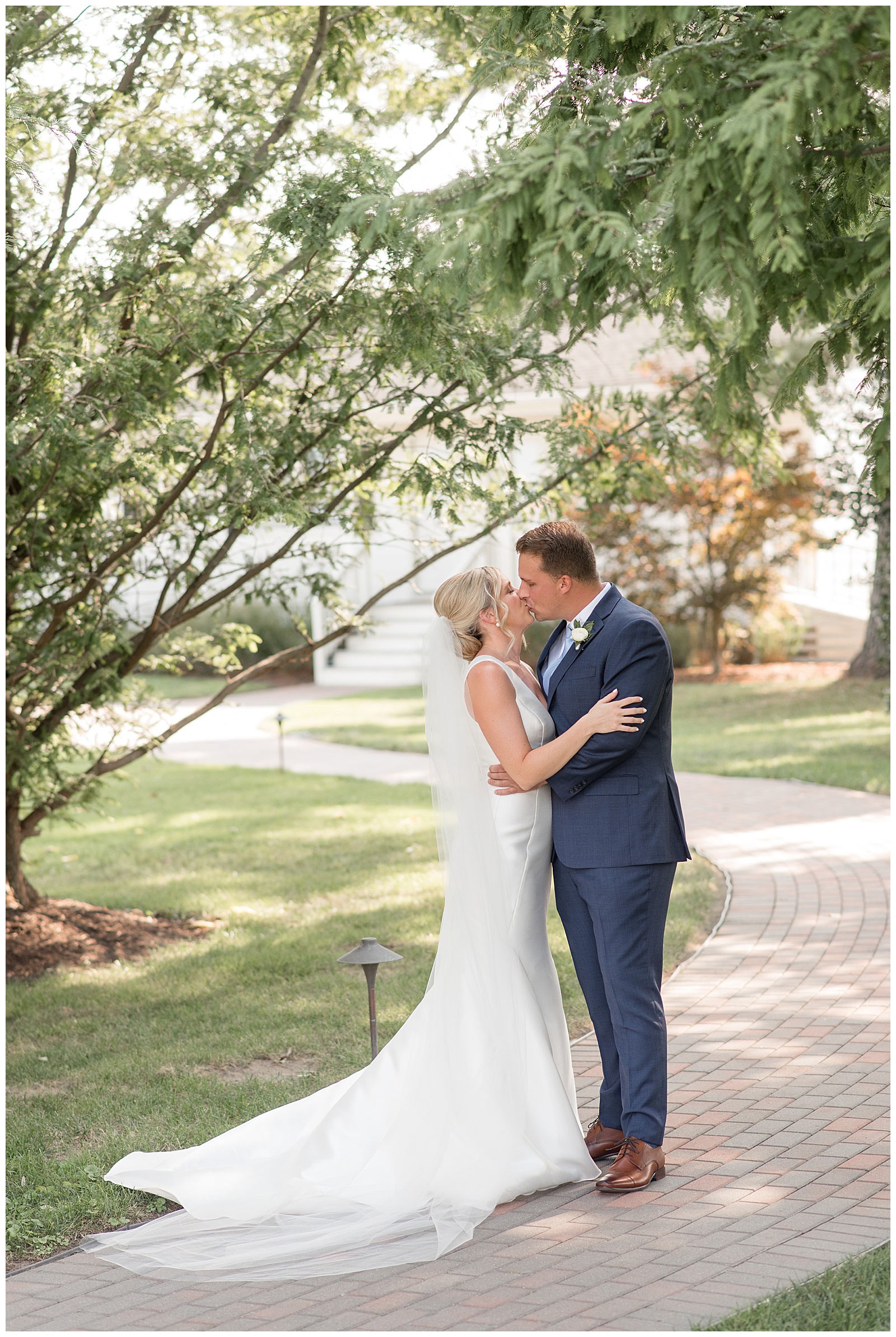 bride and groom share a kiss after their first look along paved pathway on sunny day in maryland