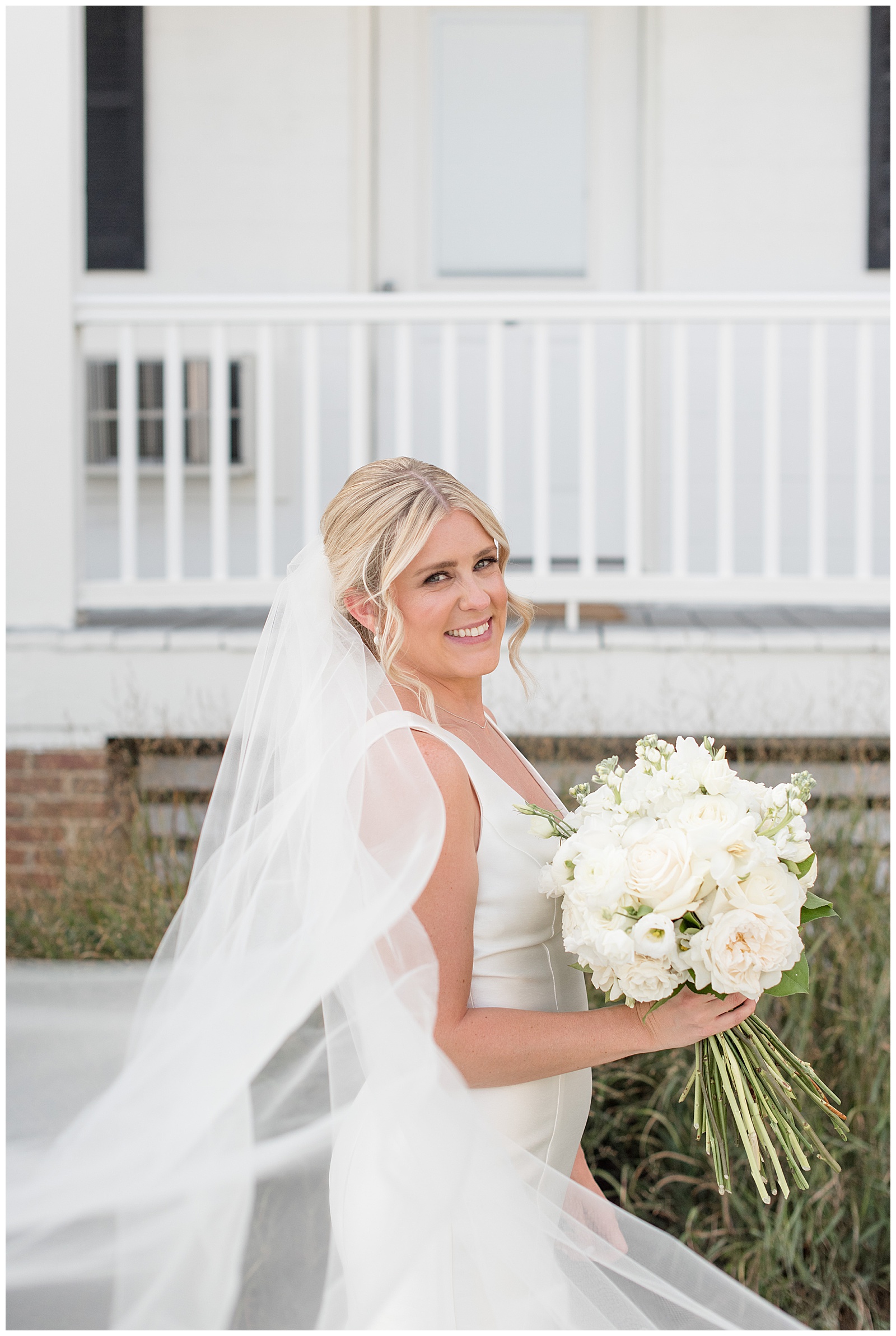 bride holding beautiful bouquet of white flowers and facing to her left by white porch on tilghman island