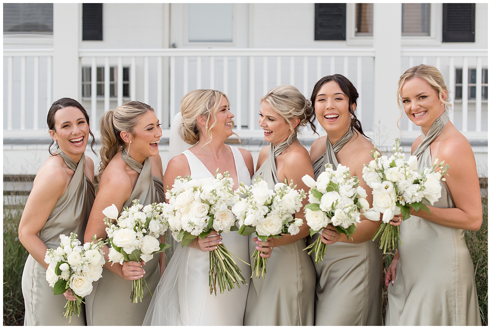 bride laughing with her bridesmaids wearing tan sleeveless gowns and all holding white bouquets on tilghman island