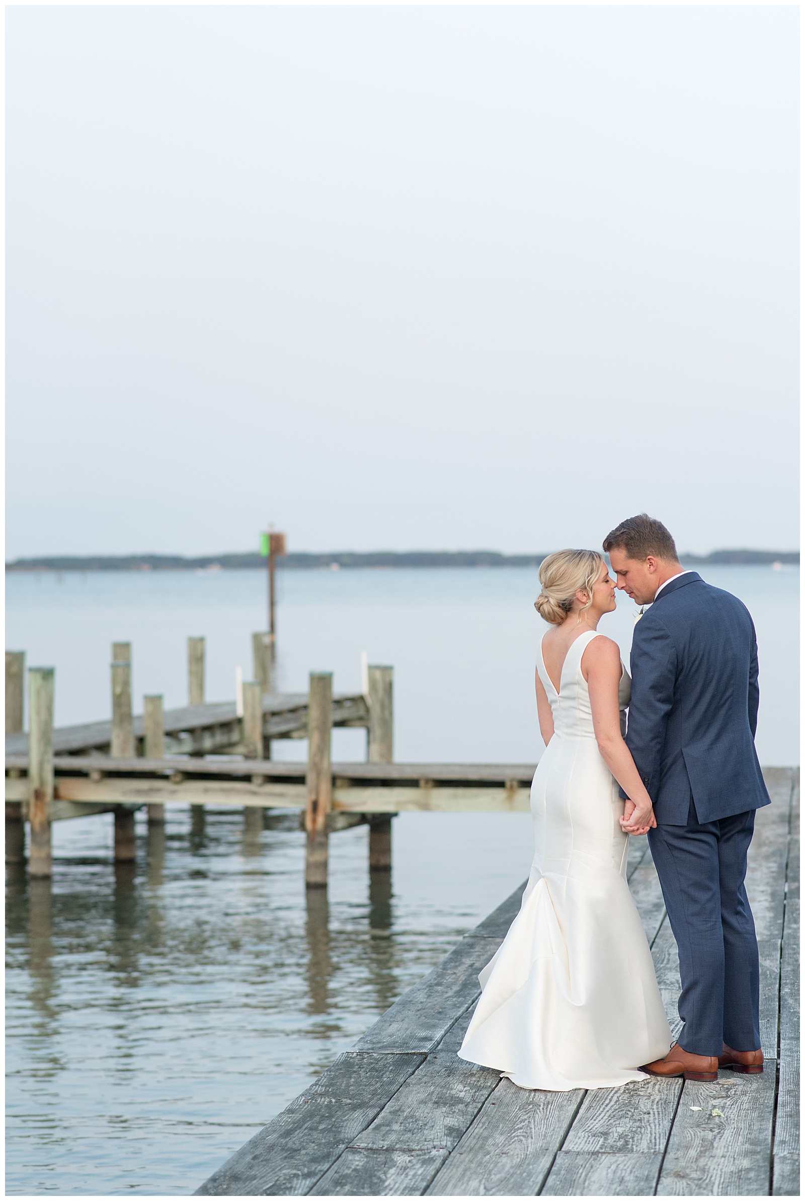 couple with backs toward camera holding hands with foreheads touching on dock at tilghman island