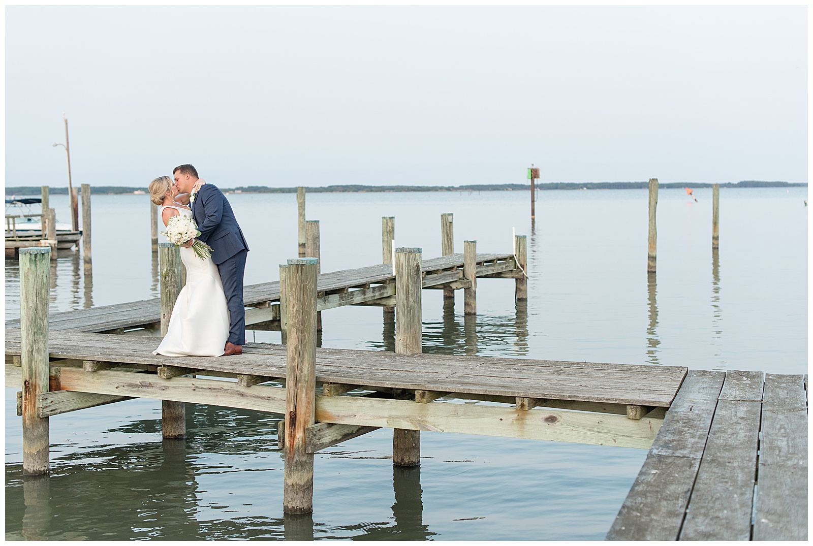 groom slightly dipping his bride back as they kiss on dock on sunny evening on tilghman island in maryland