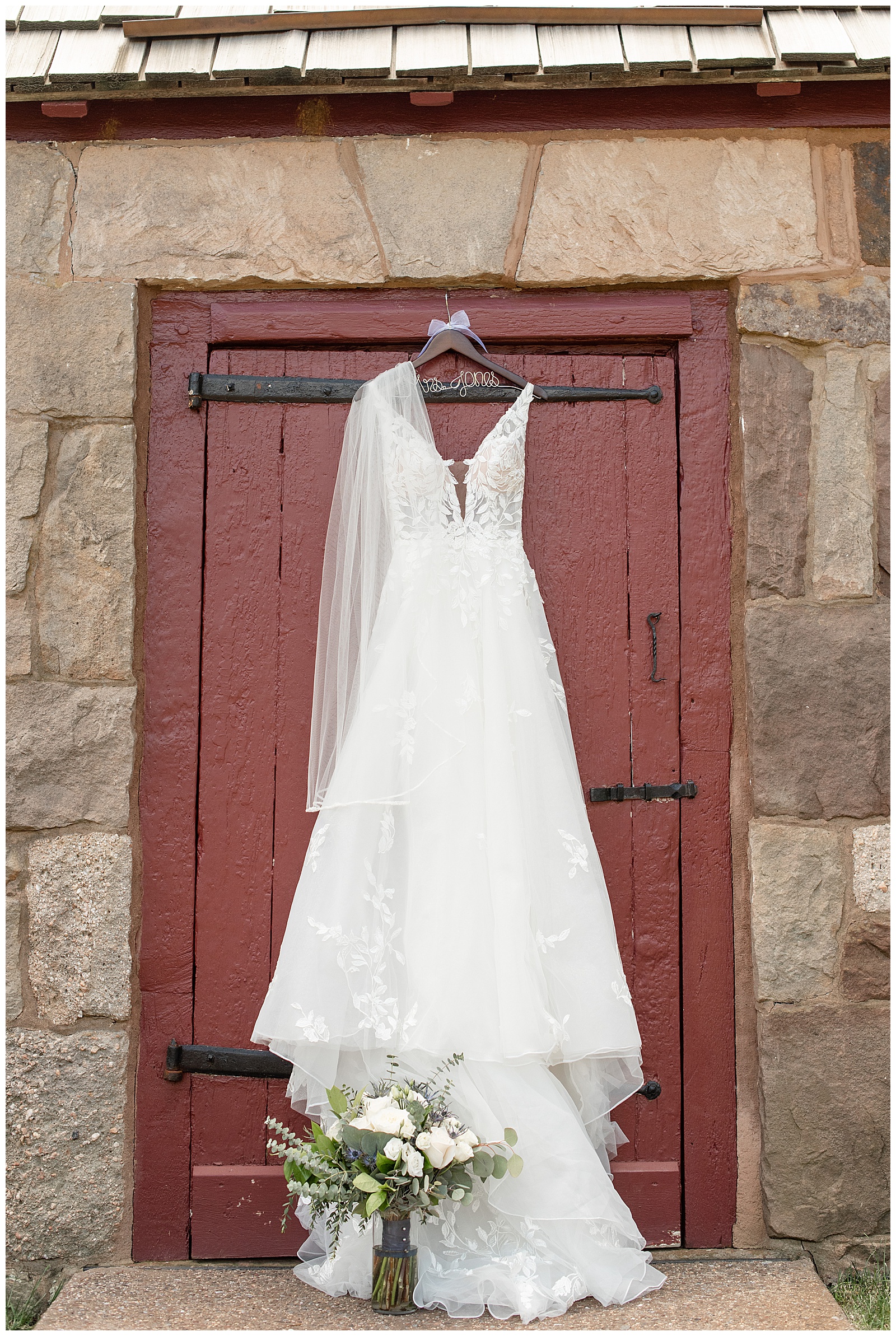 stunning white sleeveless v-neck wedding gown with white veil hanging in front of maroon barn door at elizabeth furnace