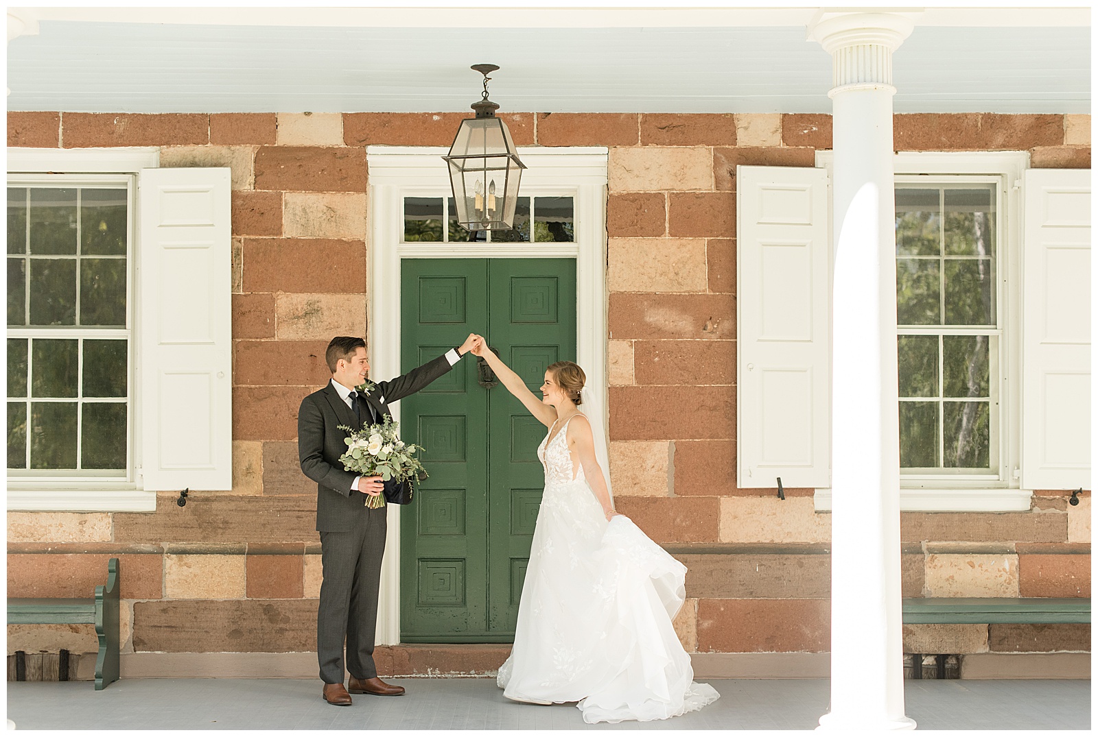 groom holding bride's bouquet as he prepares to twirl her on front porch by green door at elizabeth furnace