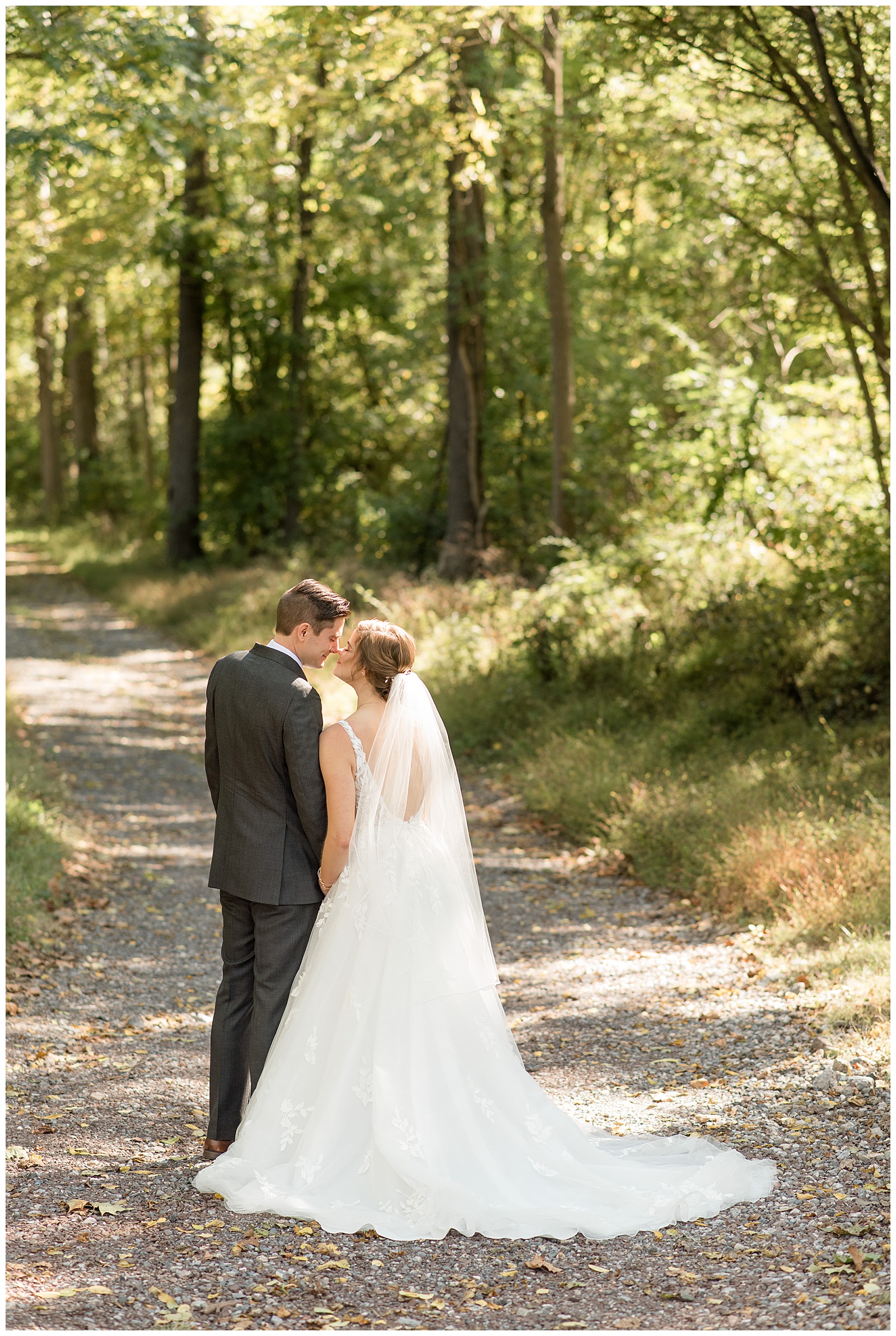 bride and groom kissing along stone path with their backs toward camera surrounded by trees in lititz pennsylvania