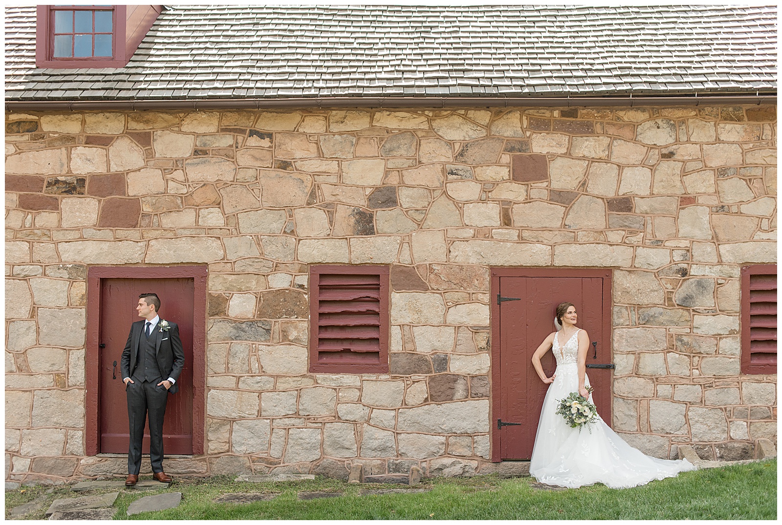 bride and groom standing far apart in front of maroon doors of stone barn and looking in opposite directions at elizabeth furnace
